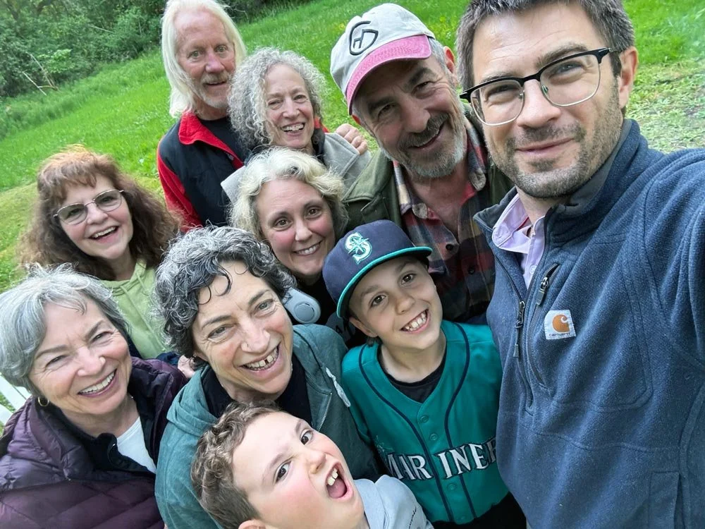 Group of ten smiling people of various ages taking a selfie outdoors on a grassy area.