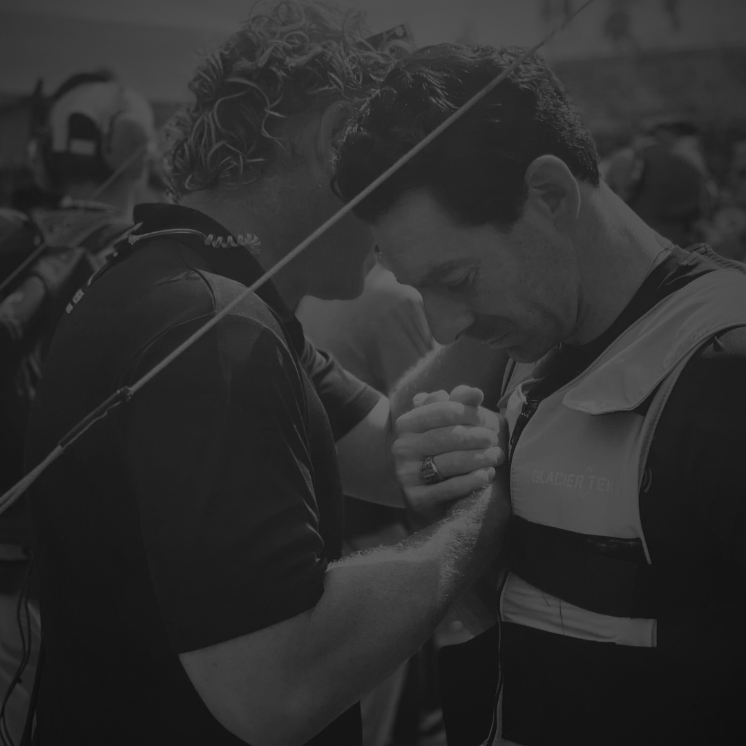 Two men praying with their foreheads pressed together during an outdoor event.