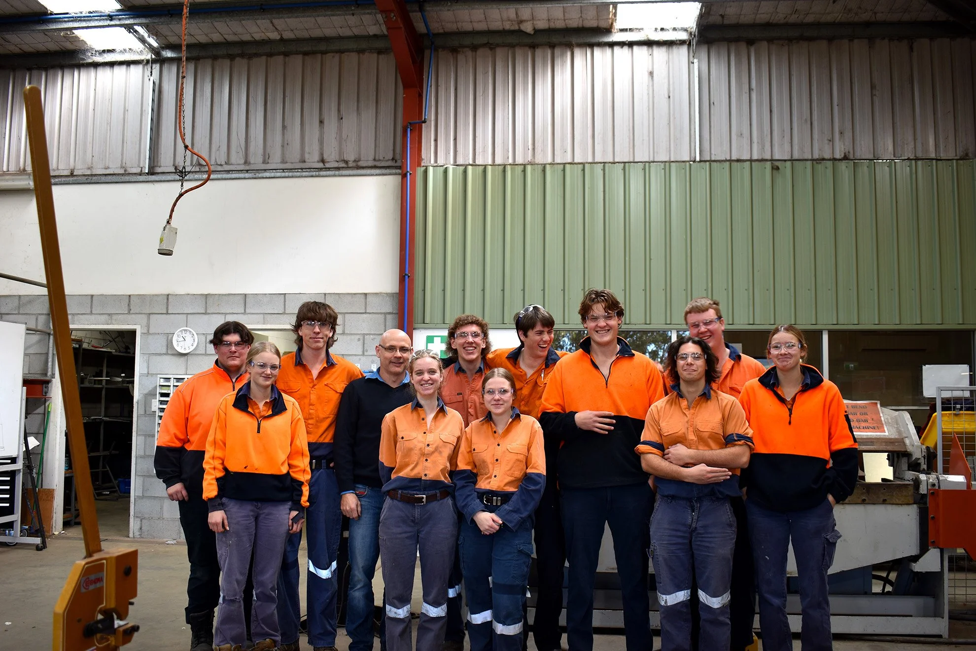 Group of people in safety uniforms smiling in an industrial workshop.