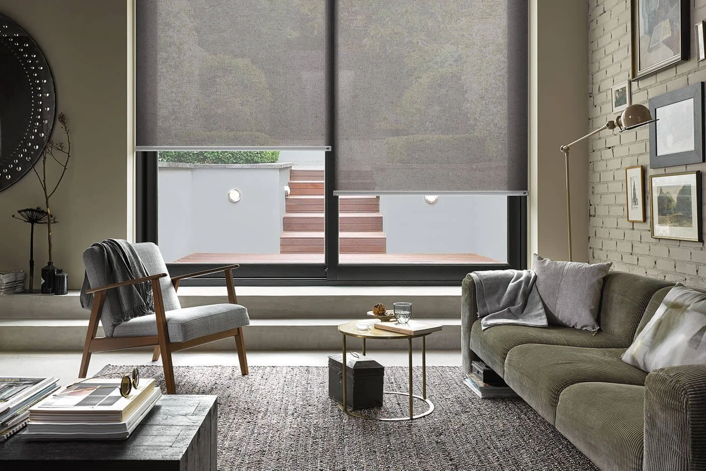Sunscreen roller blinds in grey filtering light while maintaining clear outdoor views in modern living room with exposed brick wall