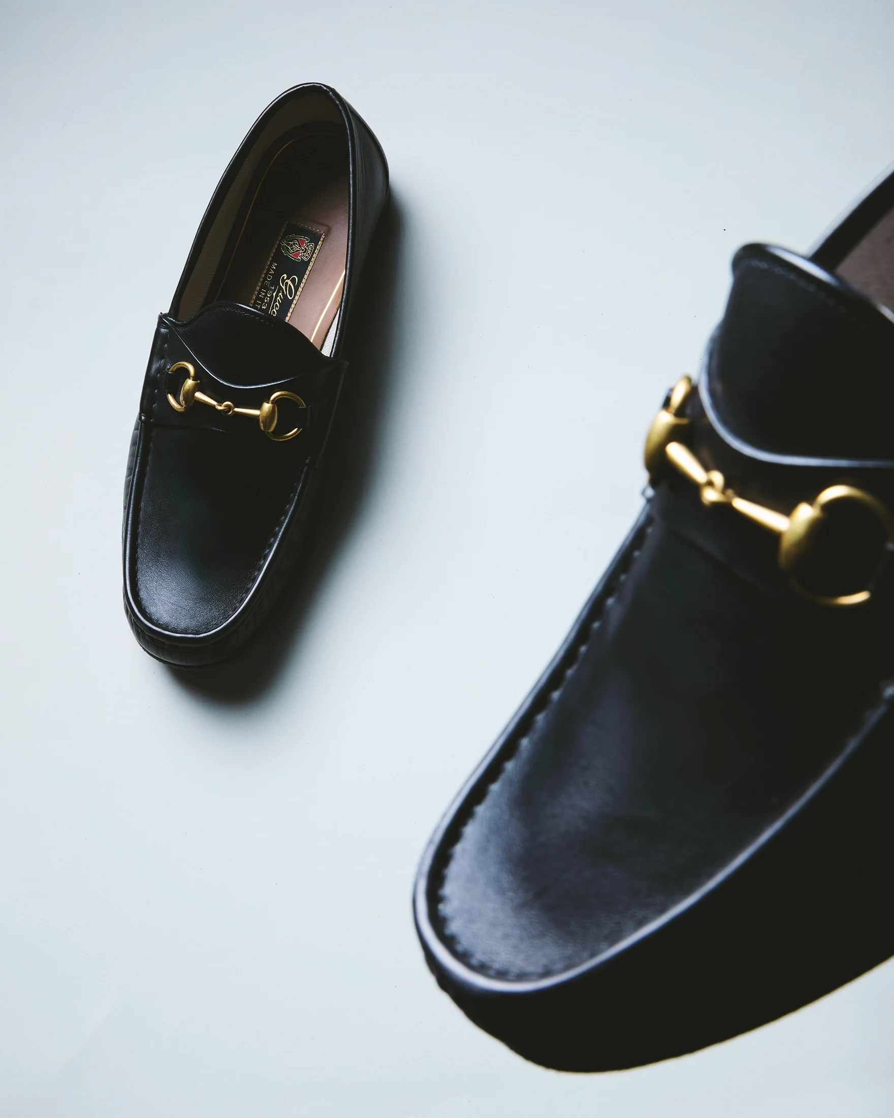Pair of black leather loafers with gold hardware on a white surface.