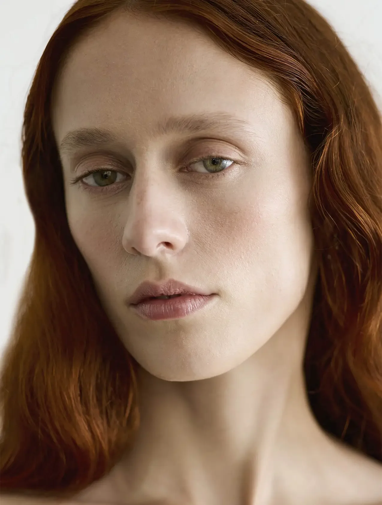 Close-up of a woman's face with red hair and light makeup, looking softly at the camera.