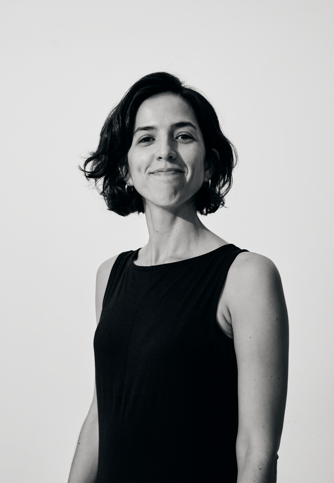 Black and white portrait of a woman with short dark hair, smiling softly, wearing a sleeveless black top against a plain background.