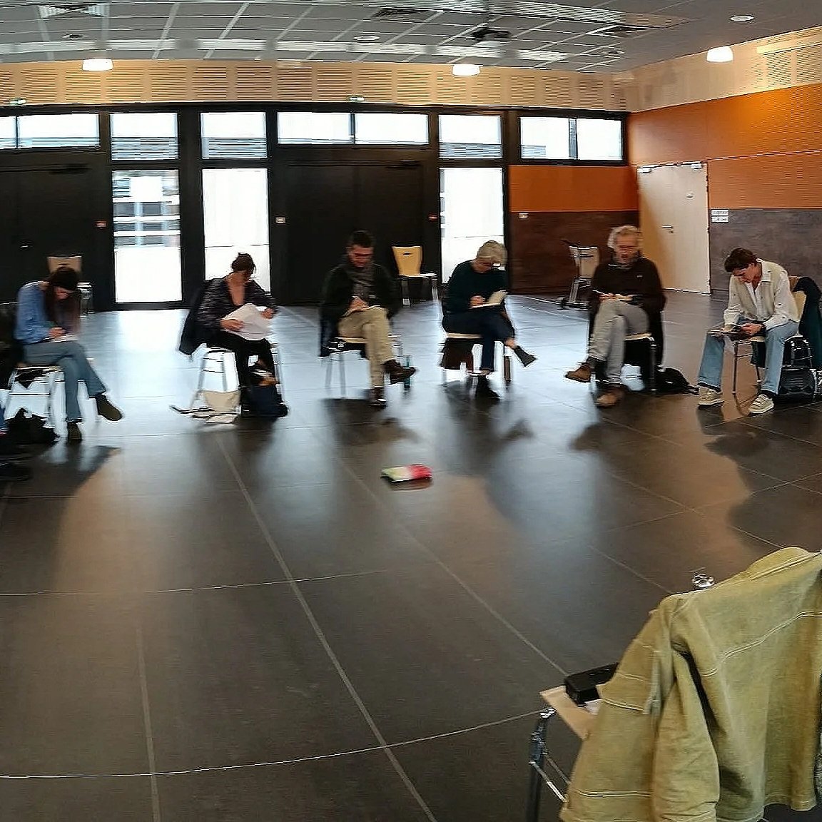 Groupe de personnes assises en ligne dans une salle d'attente ou une salle de conférence, lisant ou utilisant des appareils électroniques.