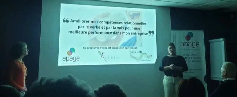 Une présentation en entreprise sur l'amélioration des compétences relationnelles, avec un écran affichant des logos d'organisations et un intervenant féminin s'adressant à un public lors d'une conférence ou formation.