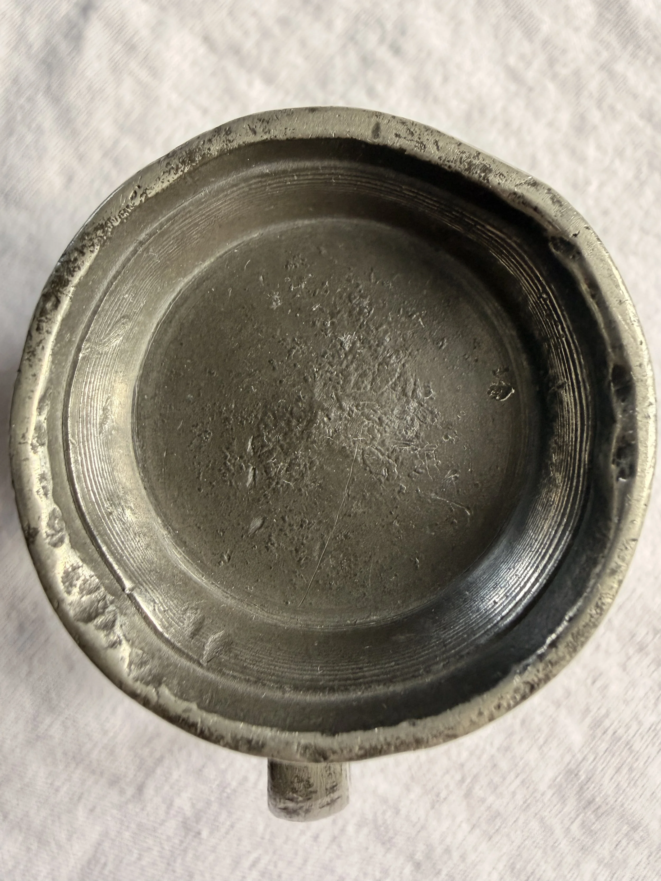 Close-up of the rim of an antique pewter measure, showing minor dints and irregularities consistent with 19th-century tavern use