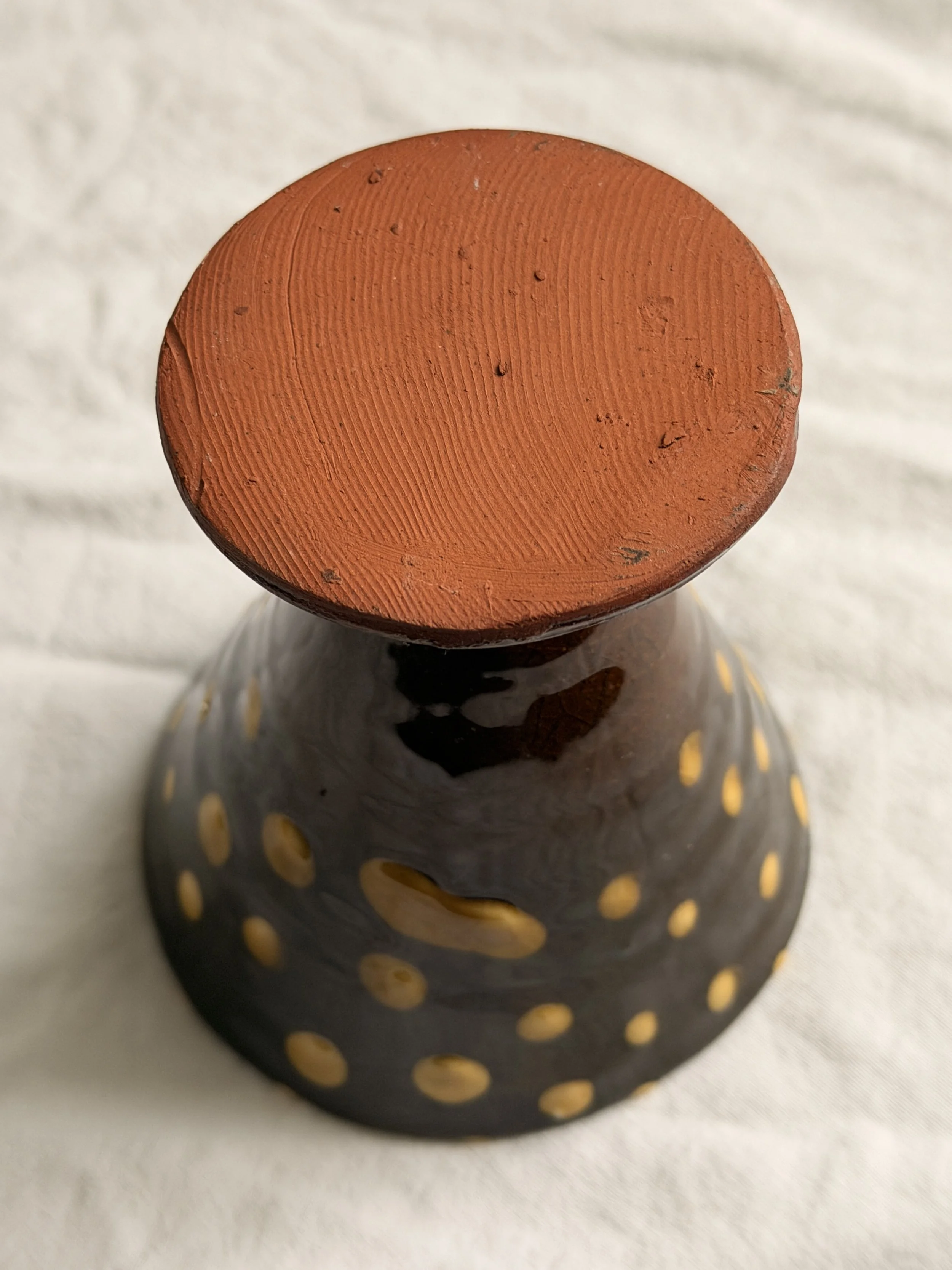Macro shot of the speckled stoneware clay and earthy glaze on a footed pottery piece.