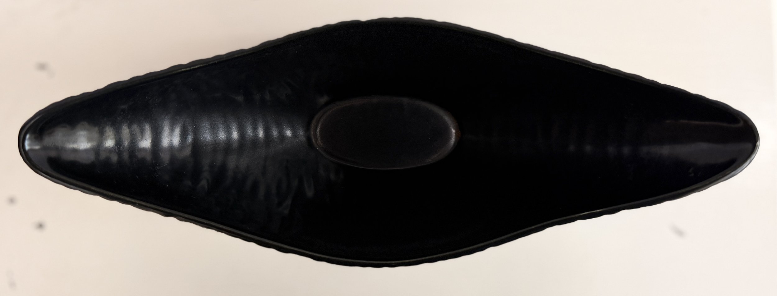 Top-down view into the wide opening of the long black gondola flower vessel.