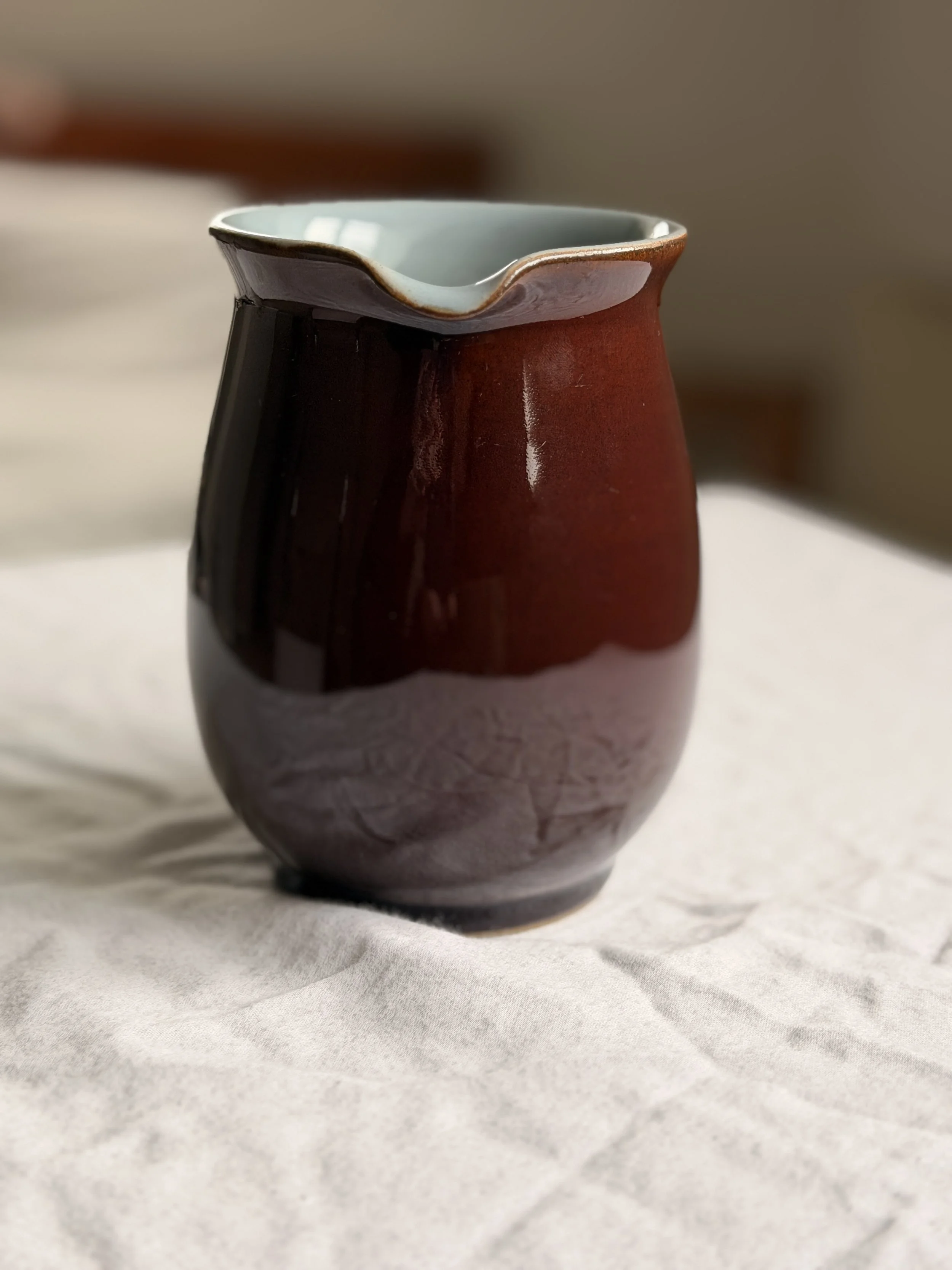 A rustic 1950s Denby brown jug used as a flower vase on a linen tablecloth