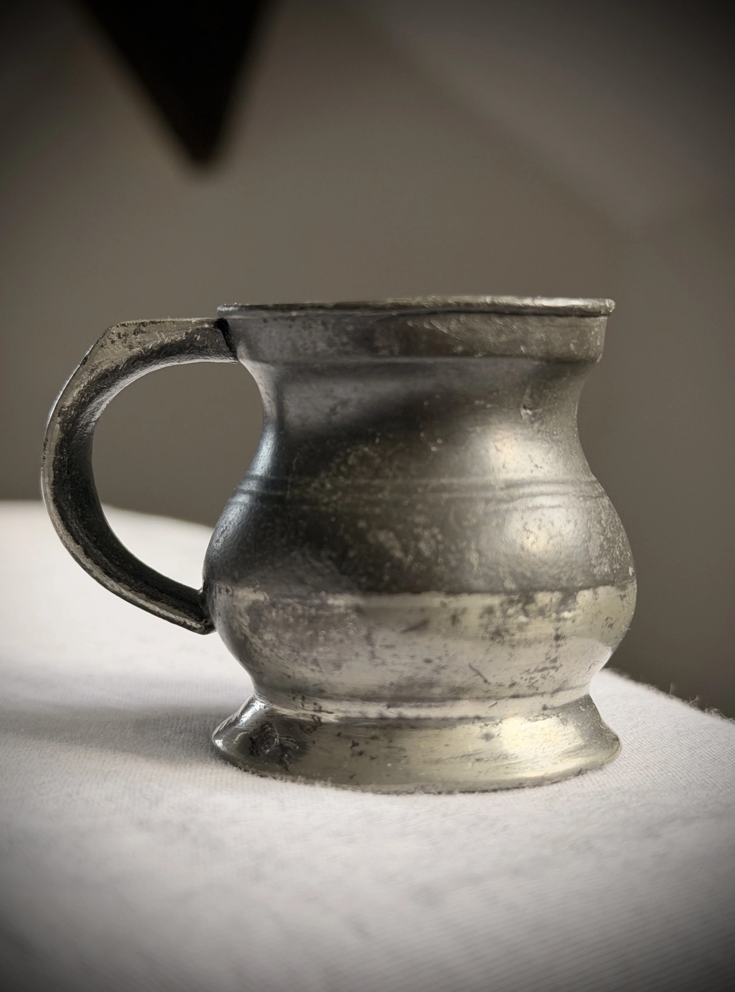 Antique 19th-century pewter 1/4 gill spirit measure with a pot-bellied shape and a thick-cast handle, showing a dark gunmetal grey patina