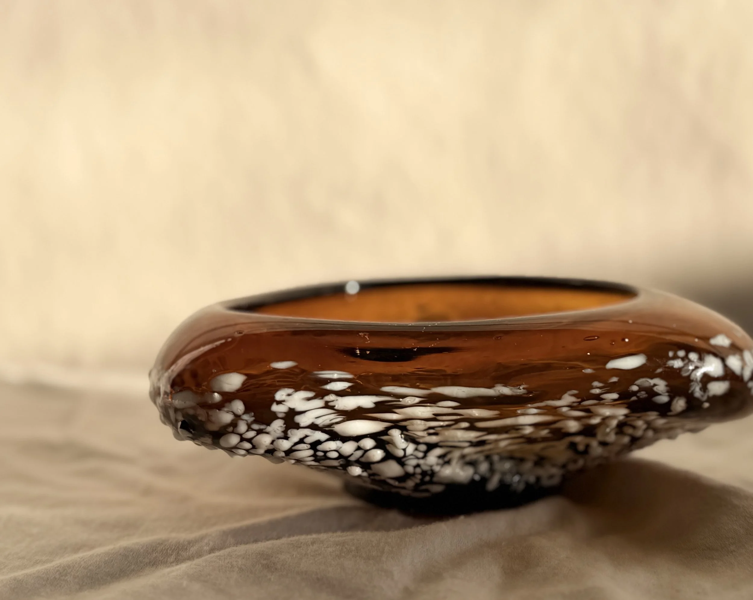 Artisanal glass bowl in warm honey tones with a matte white speckled exterior finish.