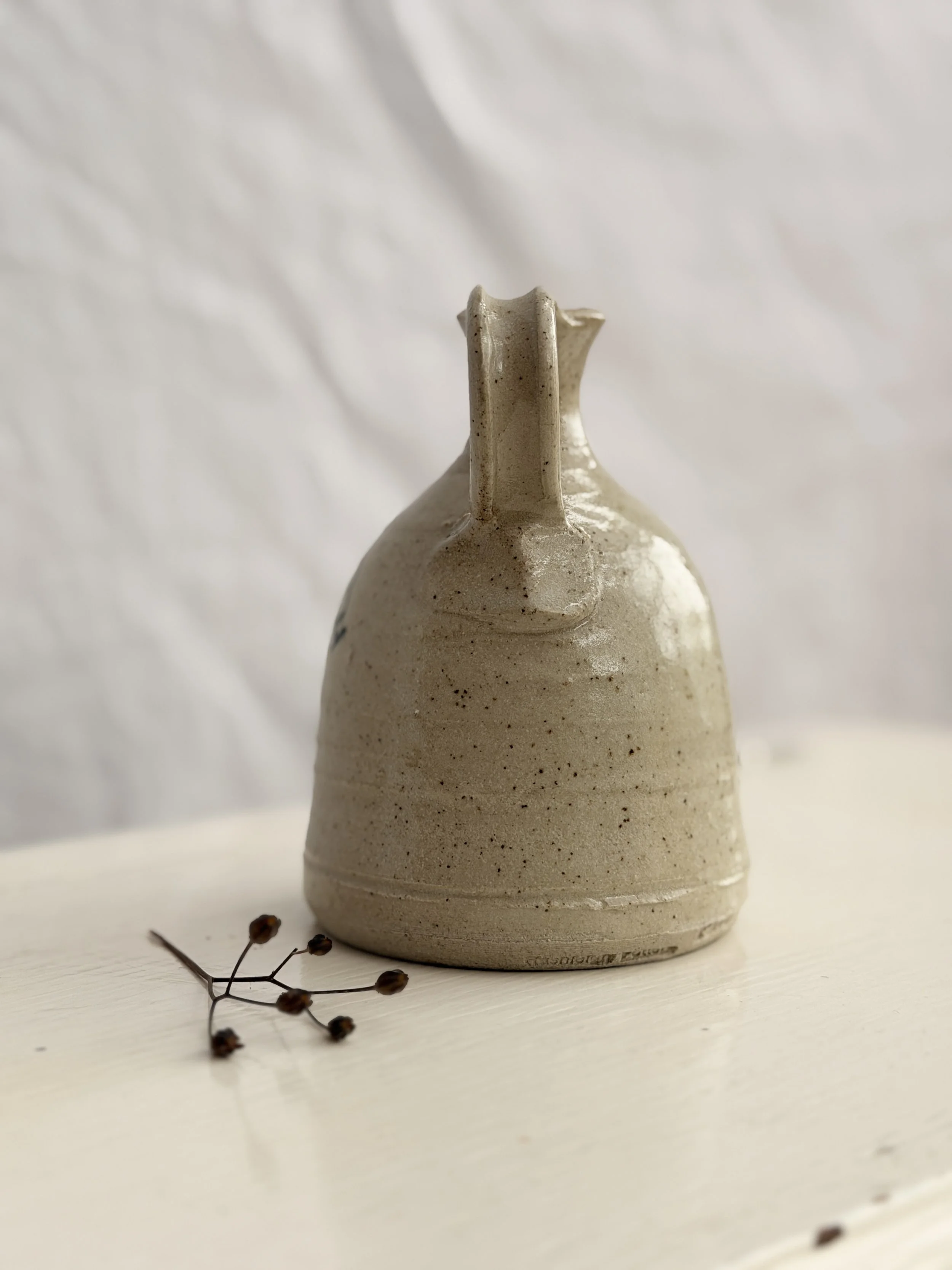 A hand-thrown studio pottery pitcher with a rustic glaze and a comfortable artisan handle.
