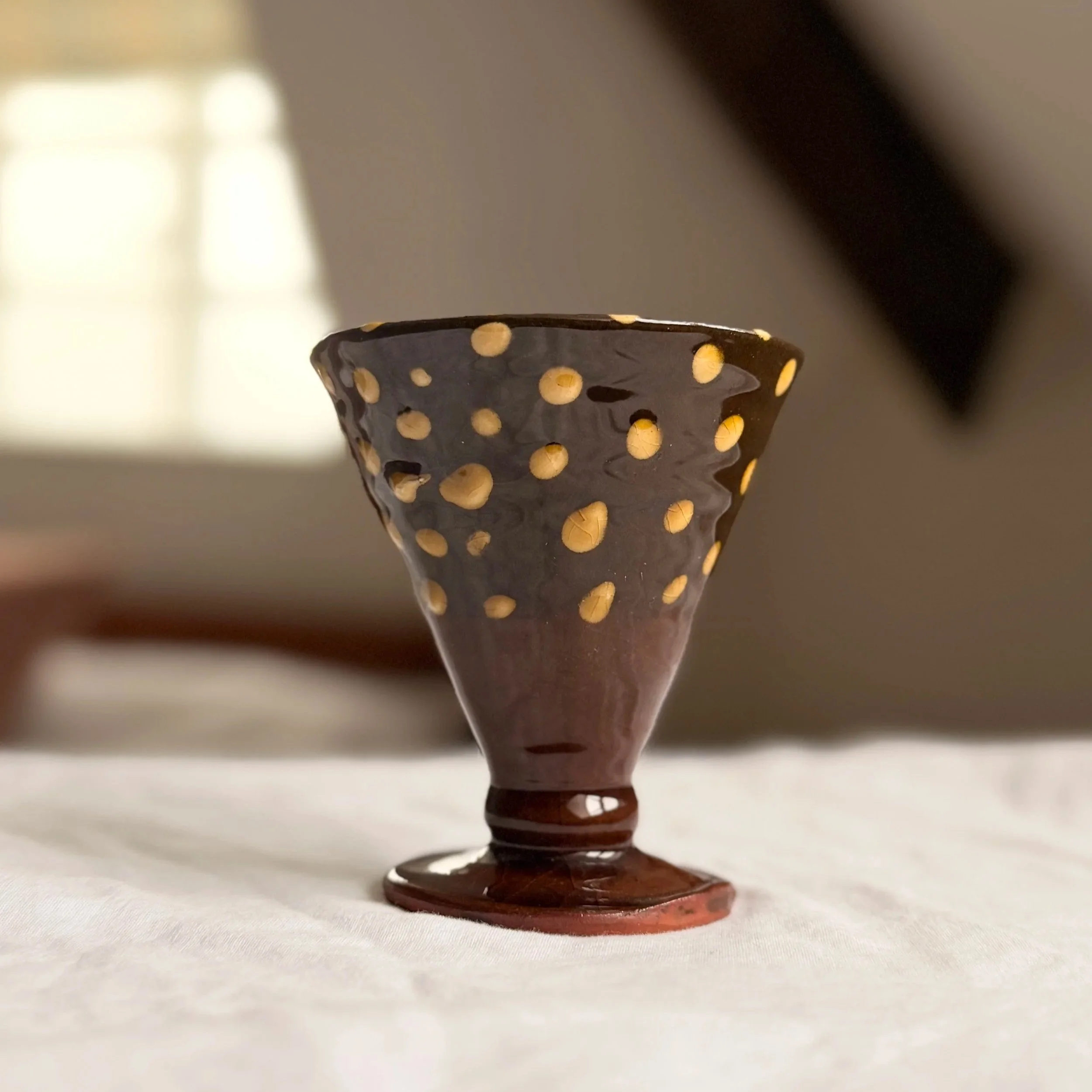 Handmade studio pottery footed chalice bowl with an earthy brown and cream polka dot slipware design.