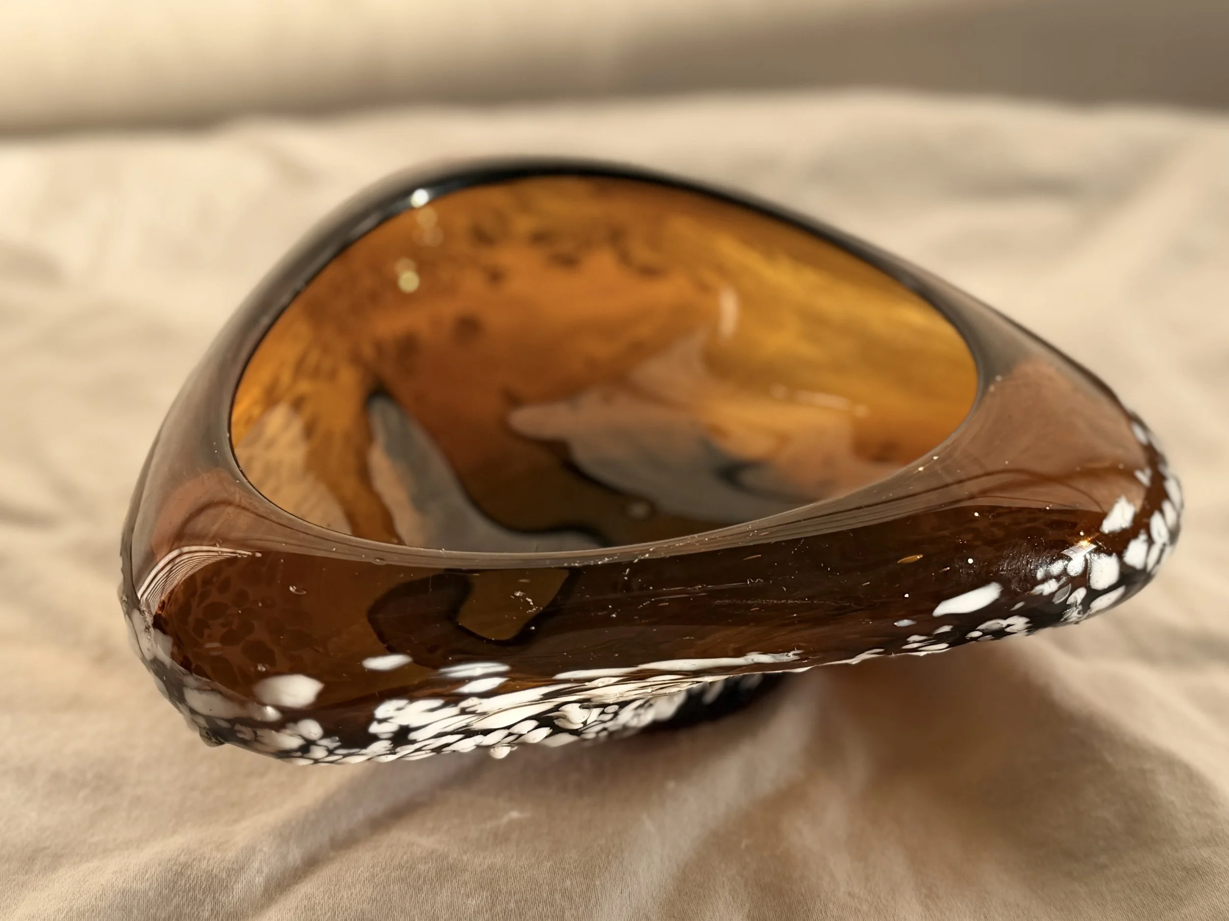 Close-up of a translucent amber glass decorative dish showing organic white frit patterns and bubbles.