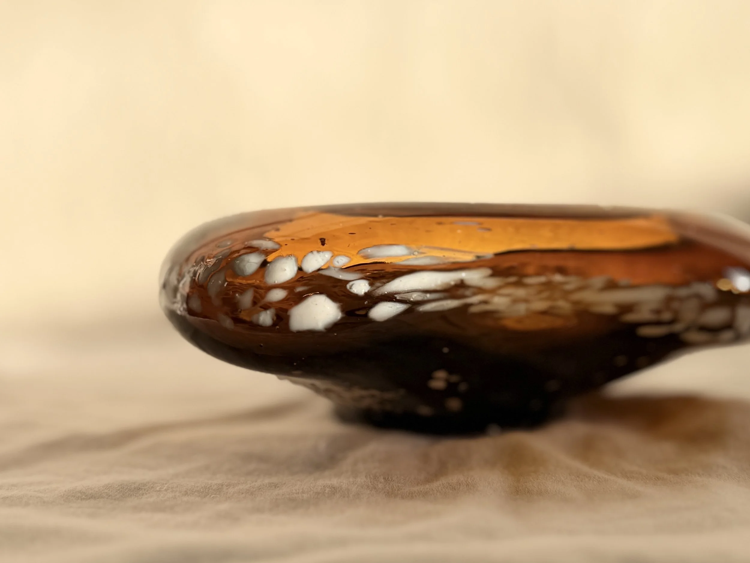 Hand-blown honey amber glass decorative bowl with white speckled frit textured exterior, displayed on a neutral linen surface.