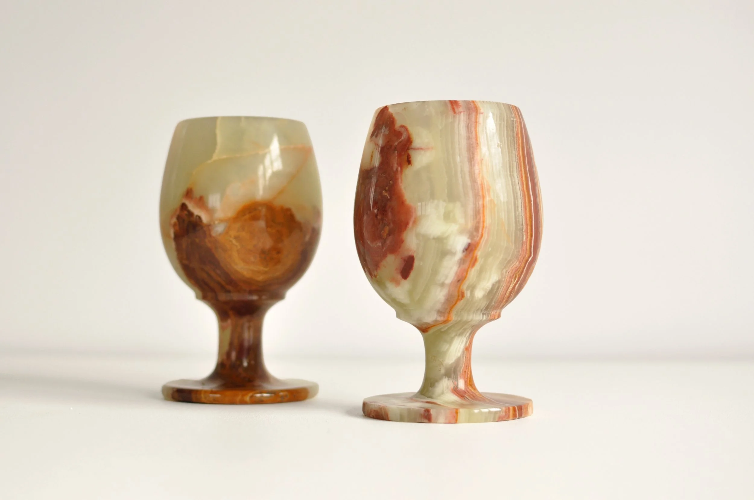 Two marble wine glasses with multicolored patterns on a white surface against a white background.