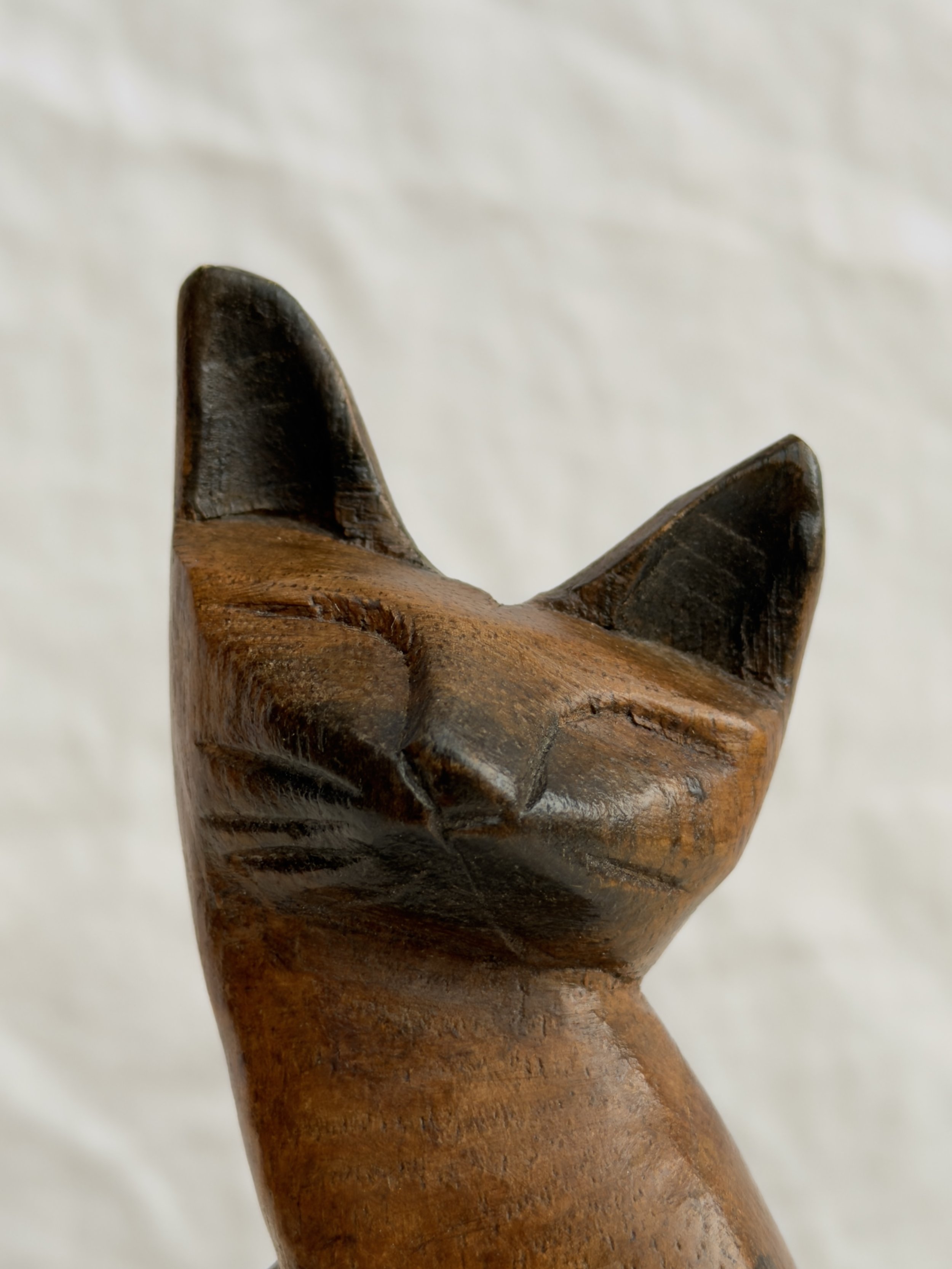 Close-up of a carved wooden cat showing the handcrafted texture and warm honey-toned wood and black ears