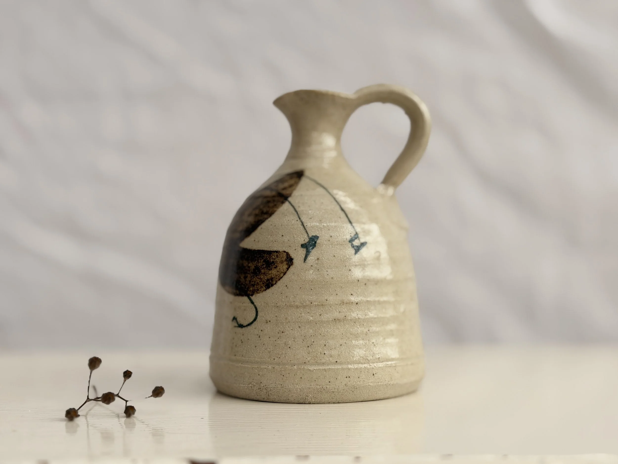 A hand-thrown studio pottery pitcher with a rustic glaze and a comfortable artisan handle.