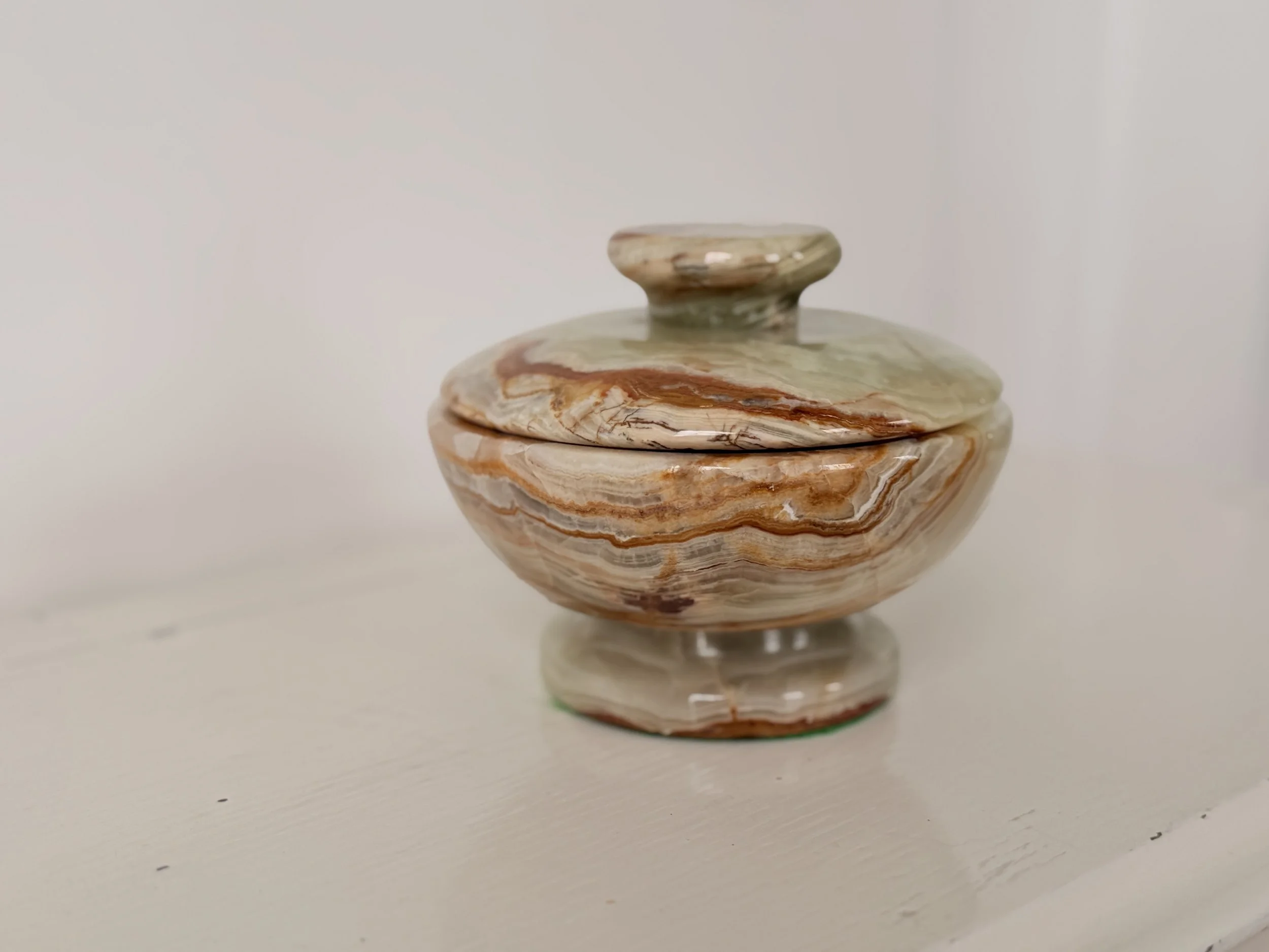 A lidded vintage trinket dish made of banded green and amber onyx stone sitting on a white mantelpiece.