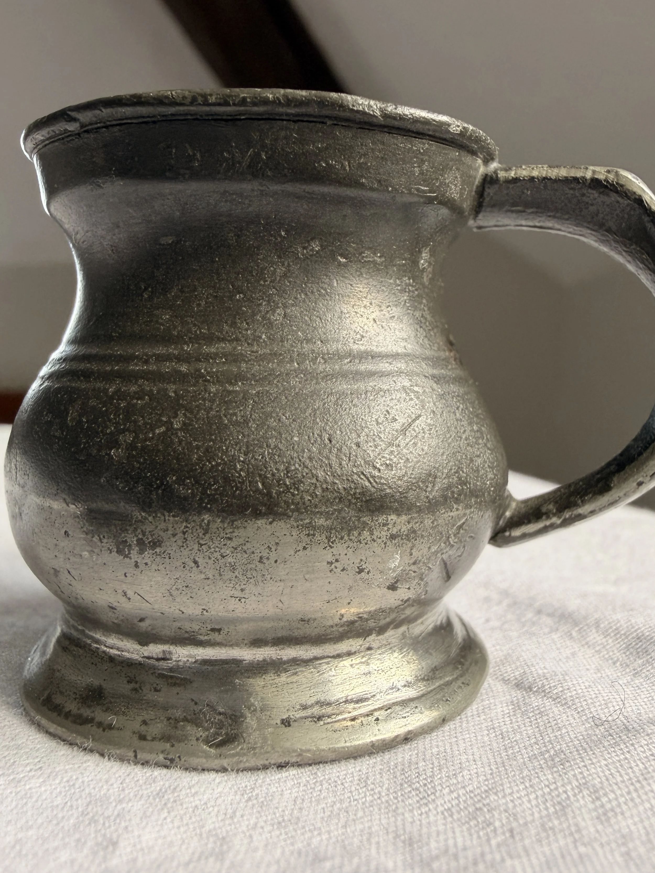 Side view of a rustic Victorian pewter tavern measure, highlighting the primitive 'noggin' design and aged metal texture