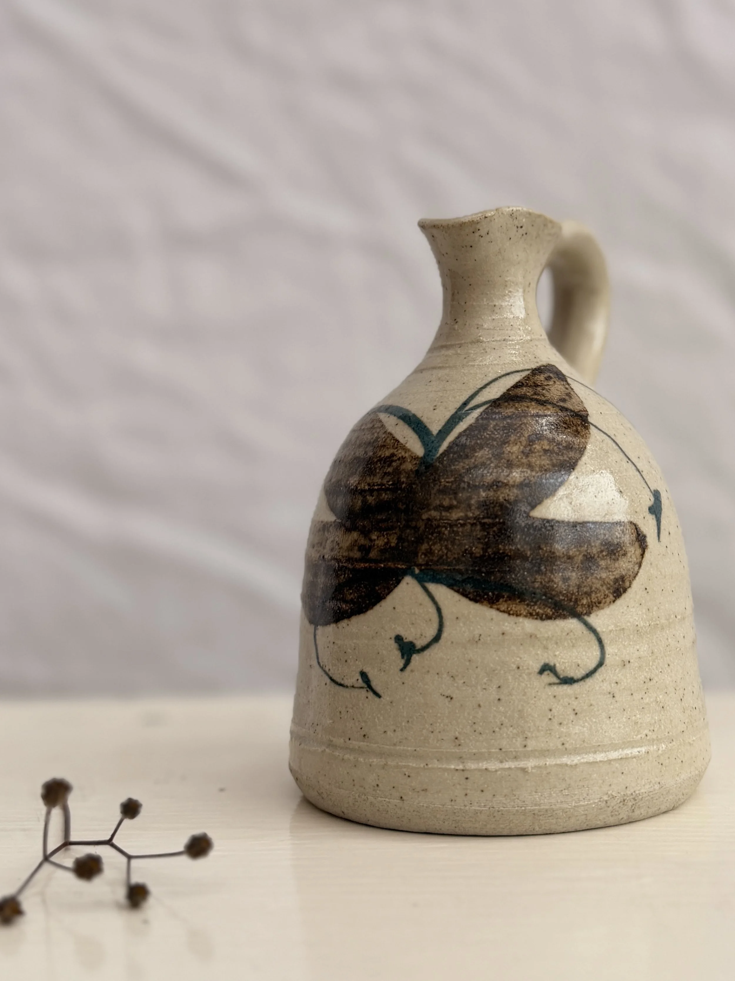 Artisan stoneware jug with a soft oatmeal glaze and blue-brown hand-painted accents.