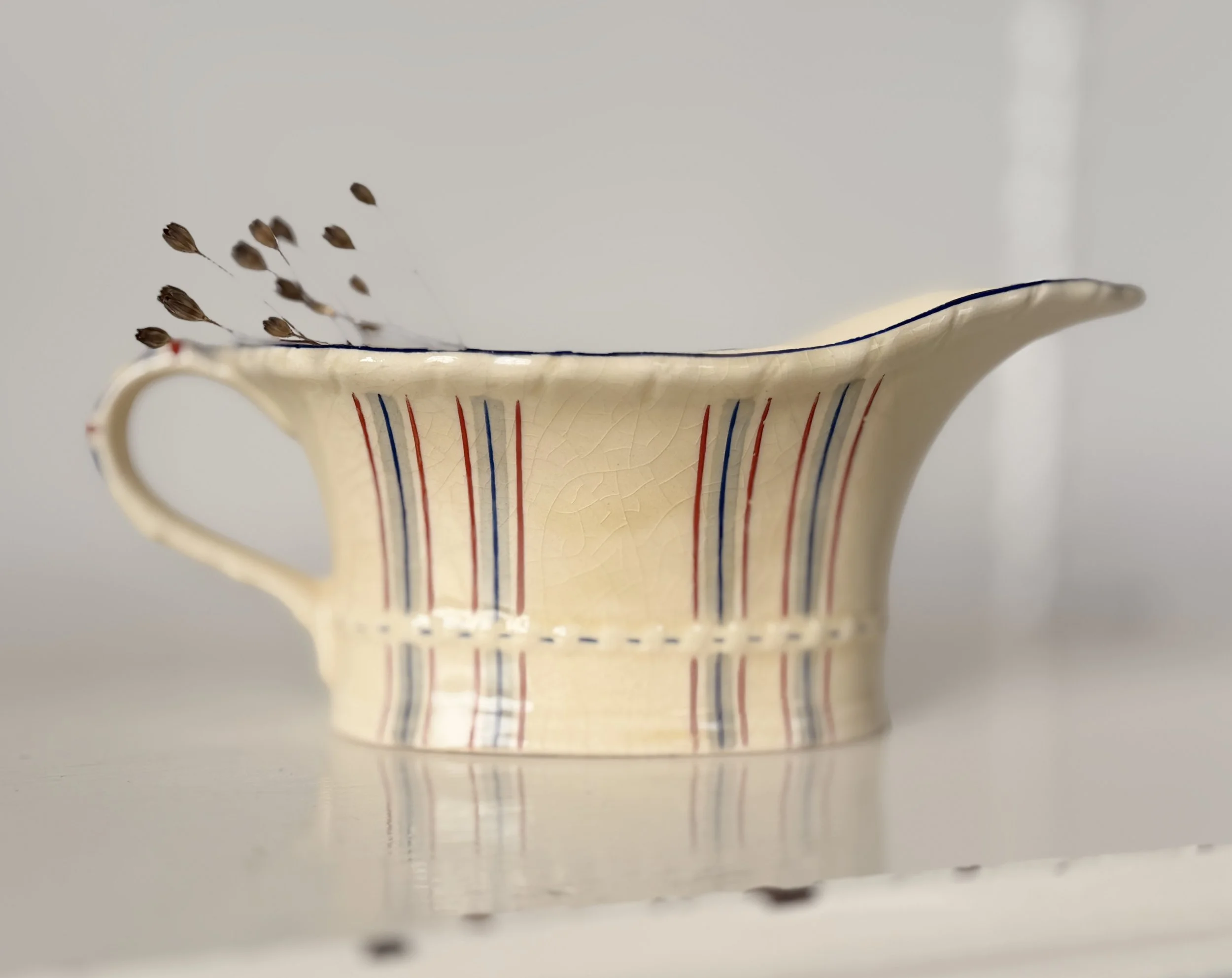 Side view of a textured, ivory-colored sauce boat reflecting soft natural light on a white shelf.