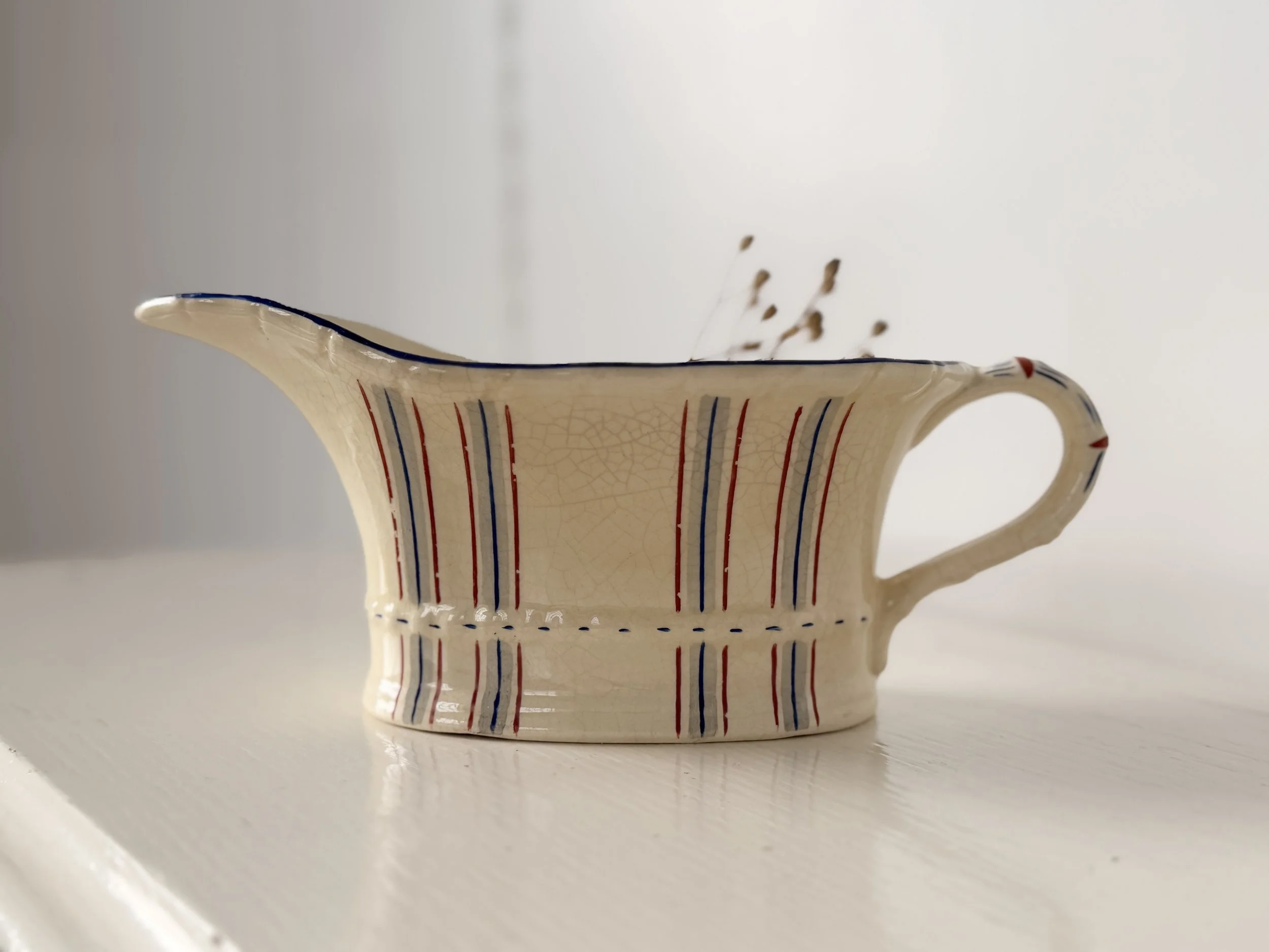 Profile shot of a ribbed creamware sauce boat with hand-painted brick red and cobalt blue vertical stripes.