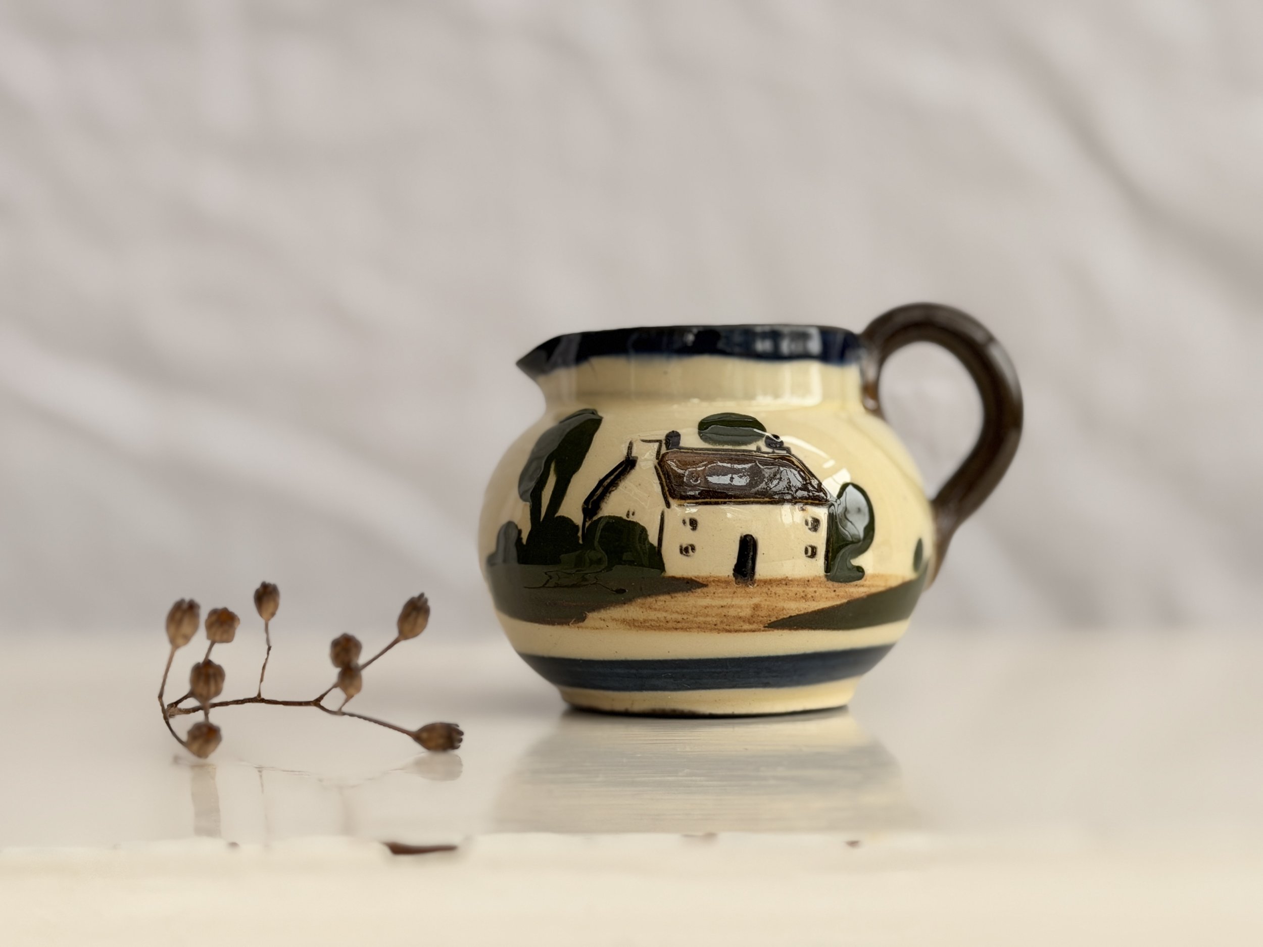 A rustic terracotta milk jug with a quaint hand-painted house, perfect for a cottagecore kitchen.