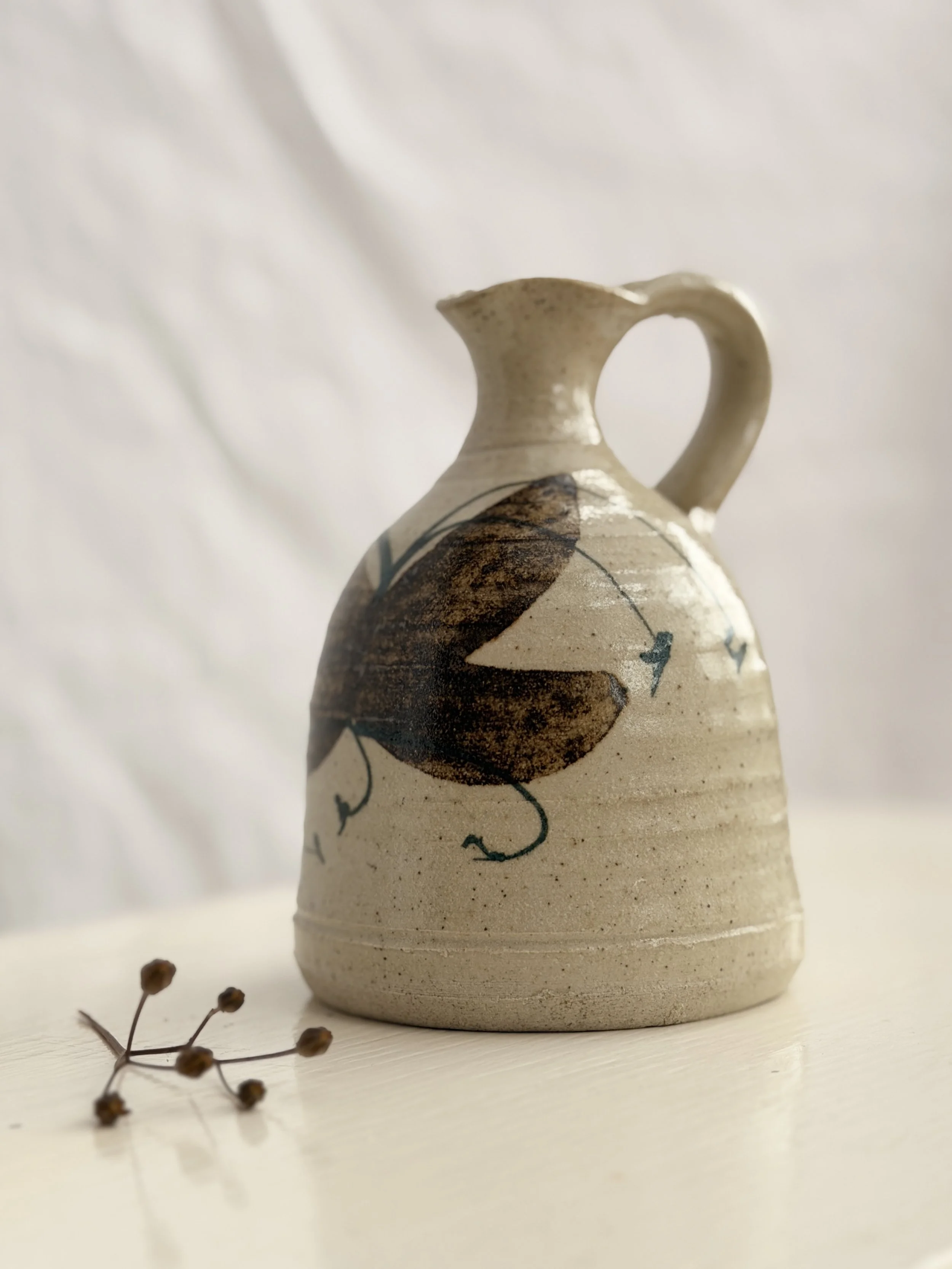 A hand-thrown studio pottery pitcher with a rustic glaze and a comfortable artisan handle.