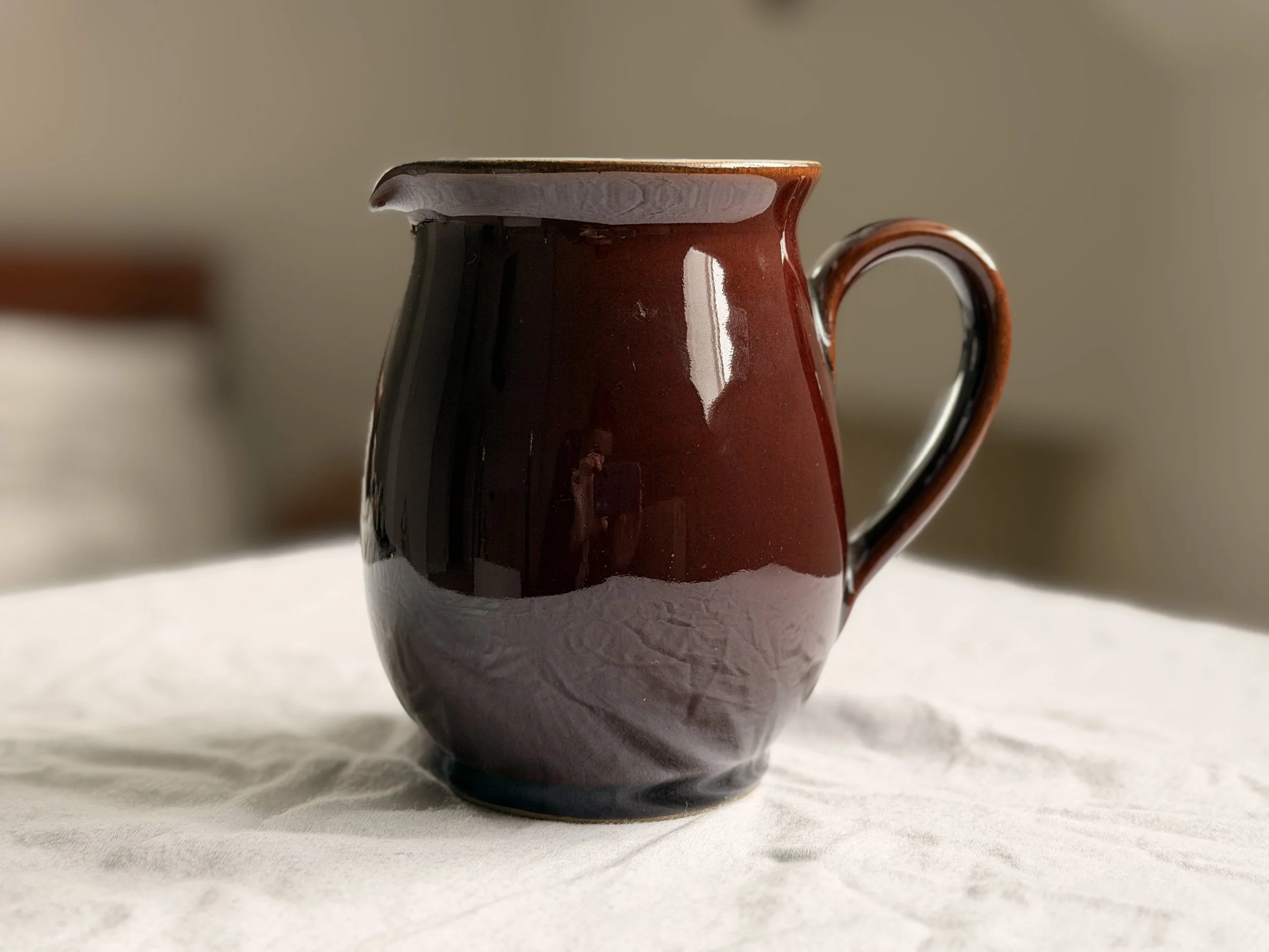 A rustic 1950s Denby brown jug used as a flower vase on a wooden farmhouse table.