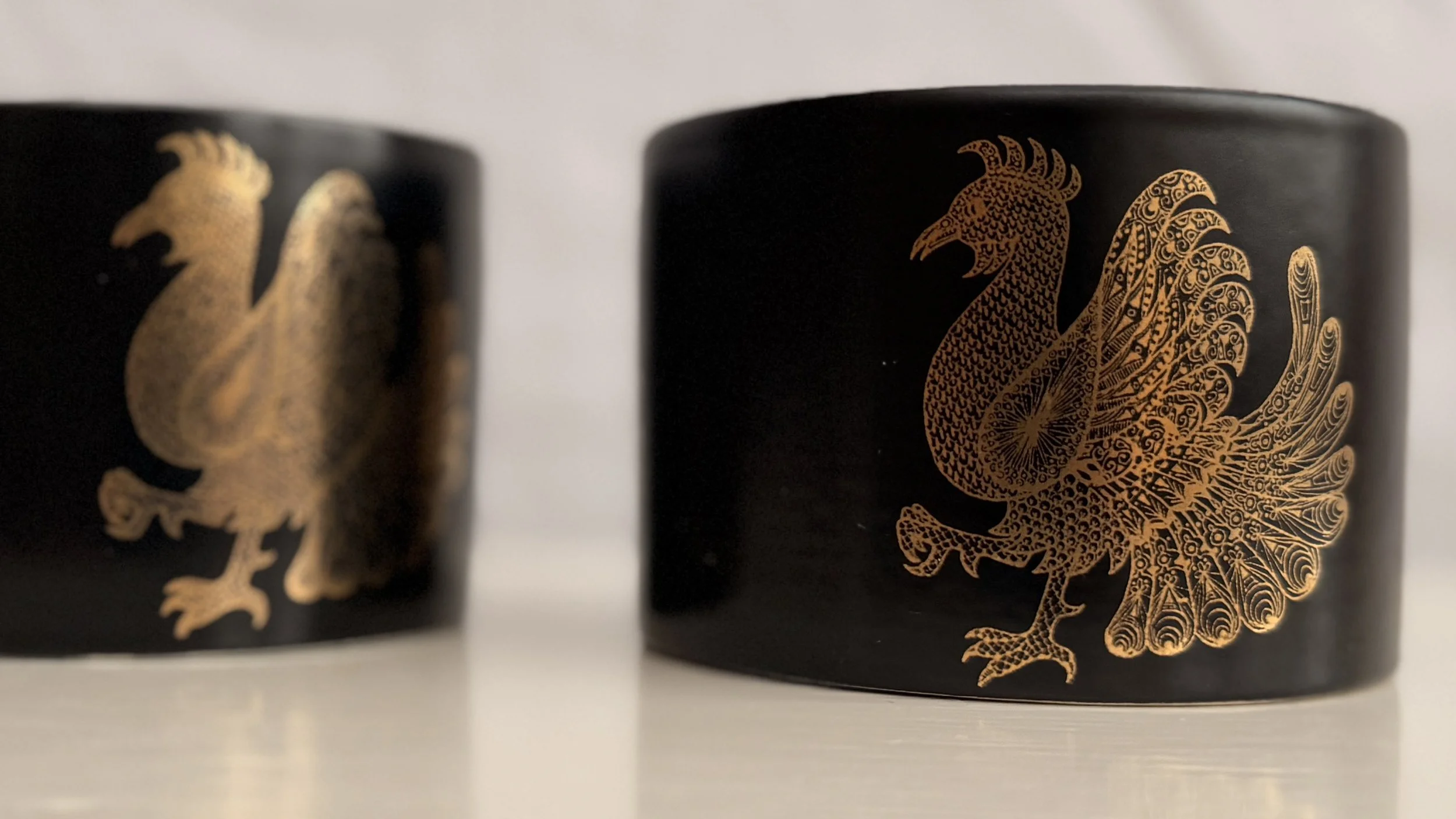 Close-up of the stylized phoenix wings in gold on the dark ceramic background.