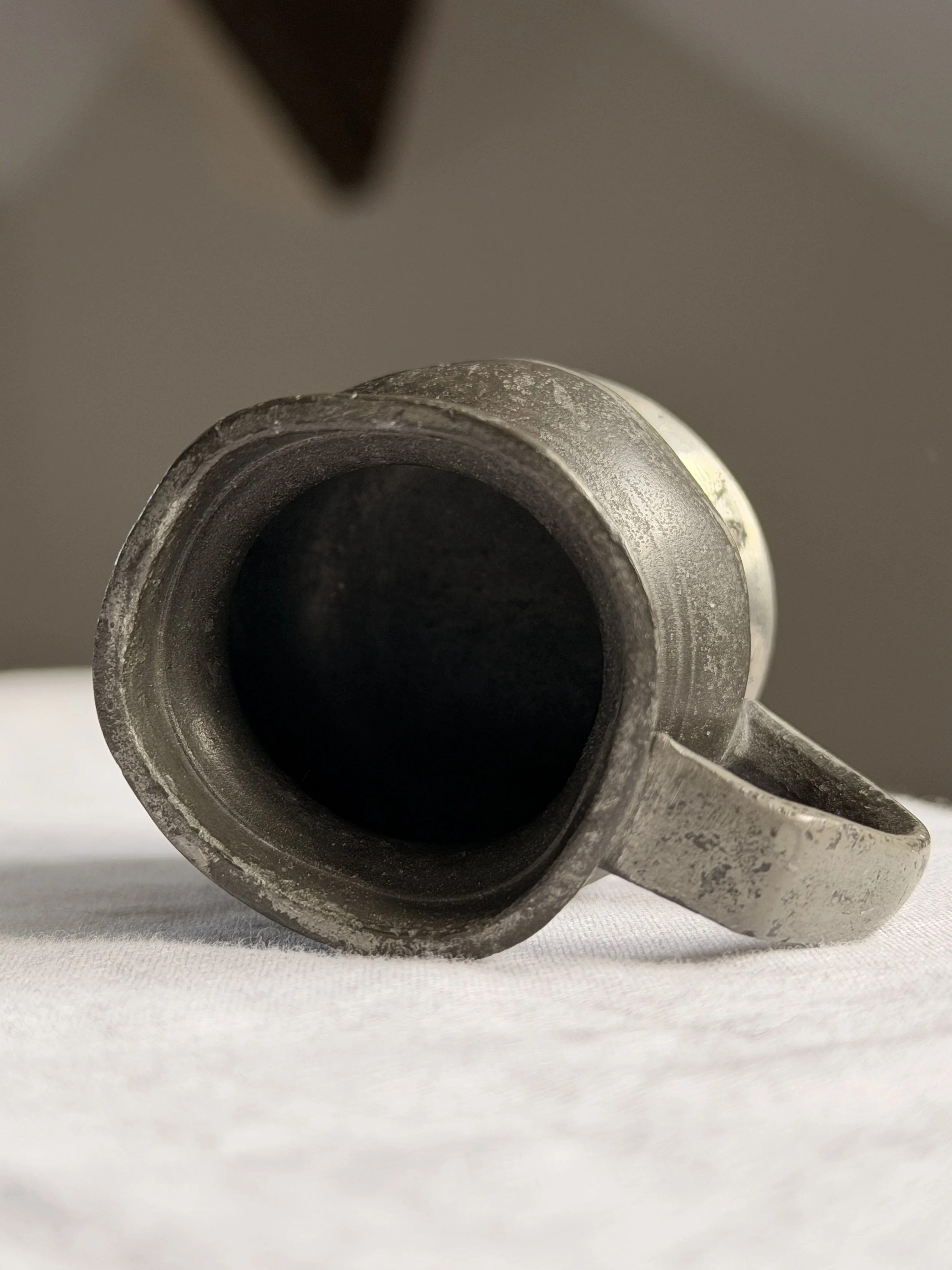 Close-up of the rim of an antique pewter measure, showing minor dints and irregularities consistent with 19th-century tavern use