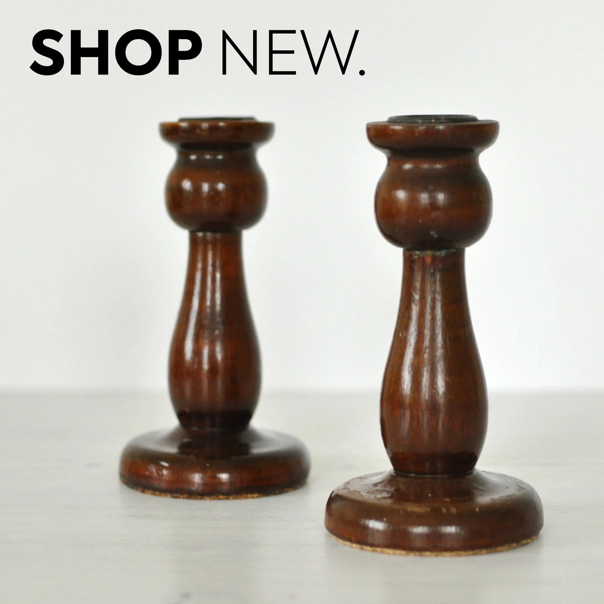 Two wooden candlesticks on a white surface against a white background, with the text "SHOP NEW." in black and bold at the top left corner.