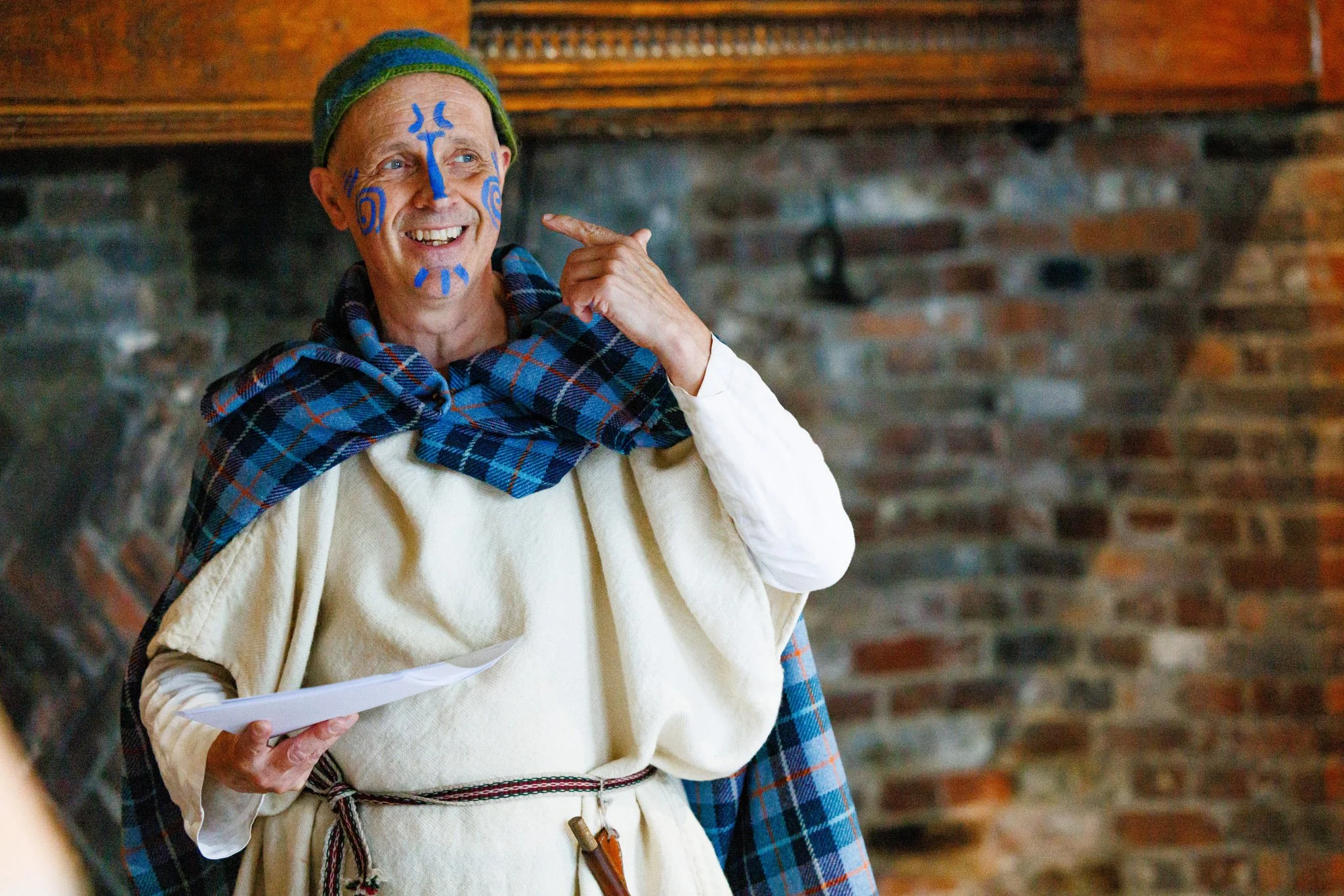 An Iron Age man with blue wode painted on his face points at the wode and smiles.