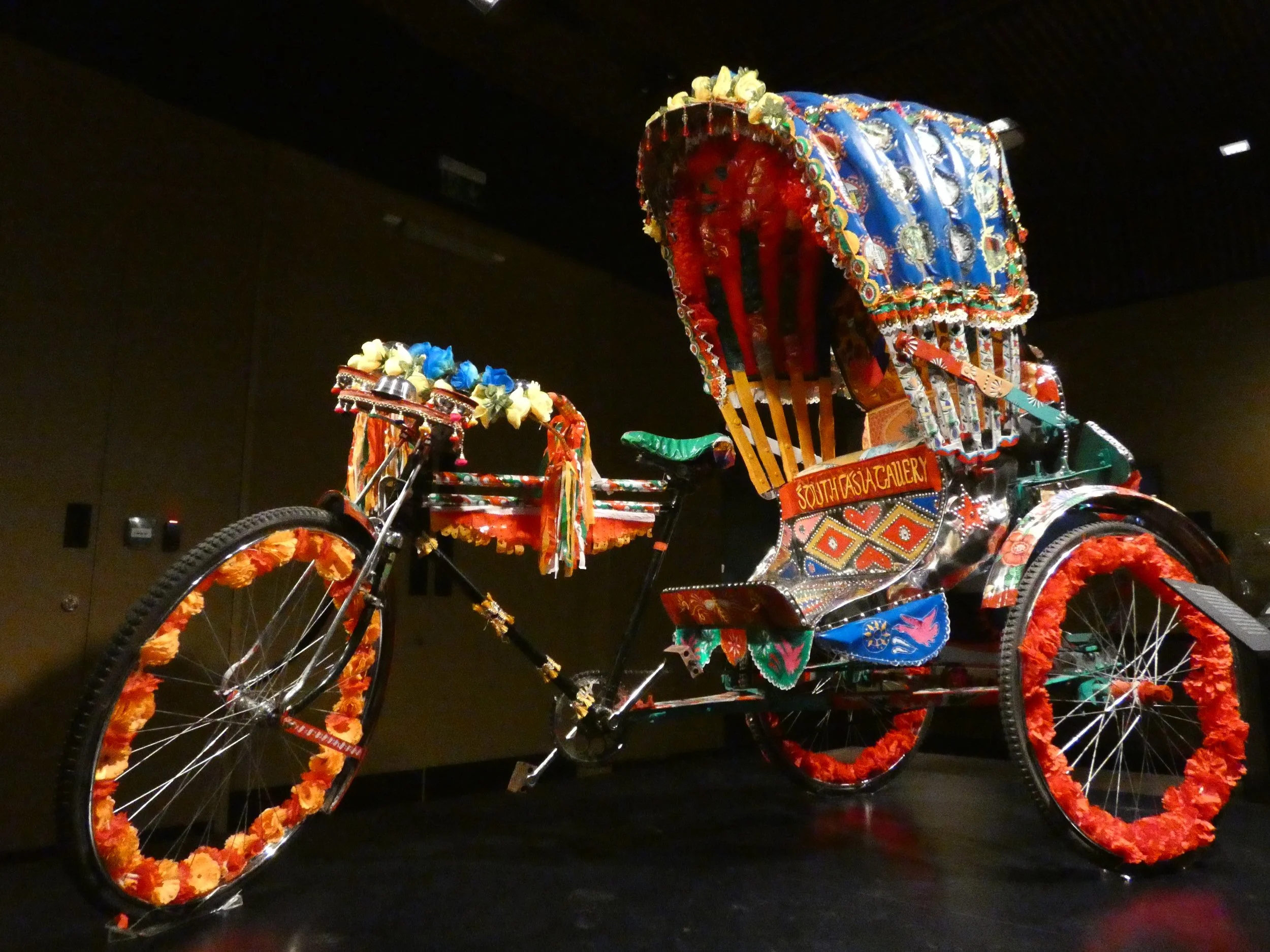 Colorful, decorative rickshaw with floral patterns and vibrant designs on display indoors.