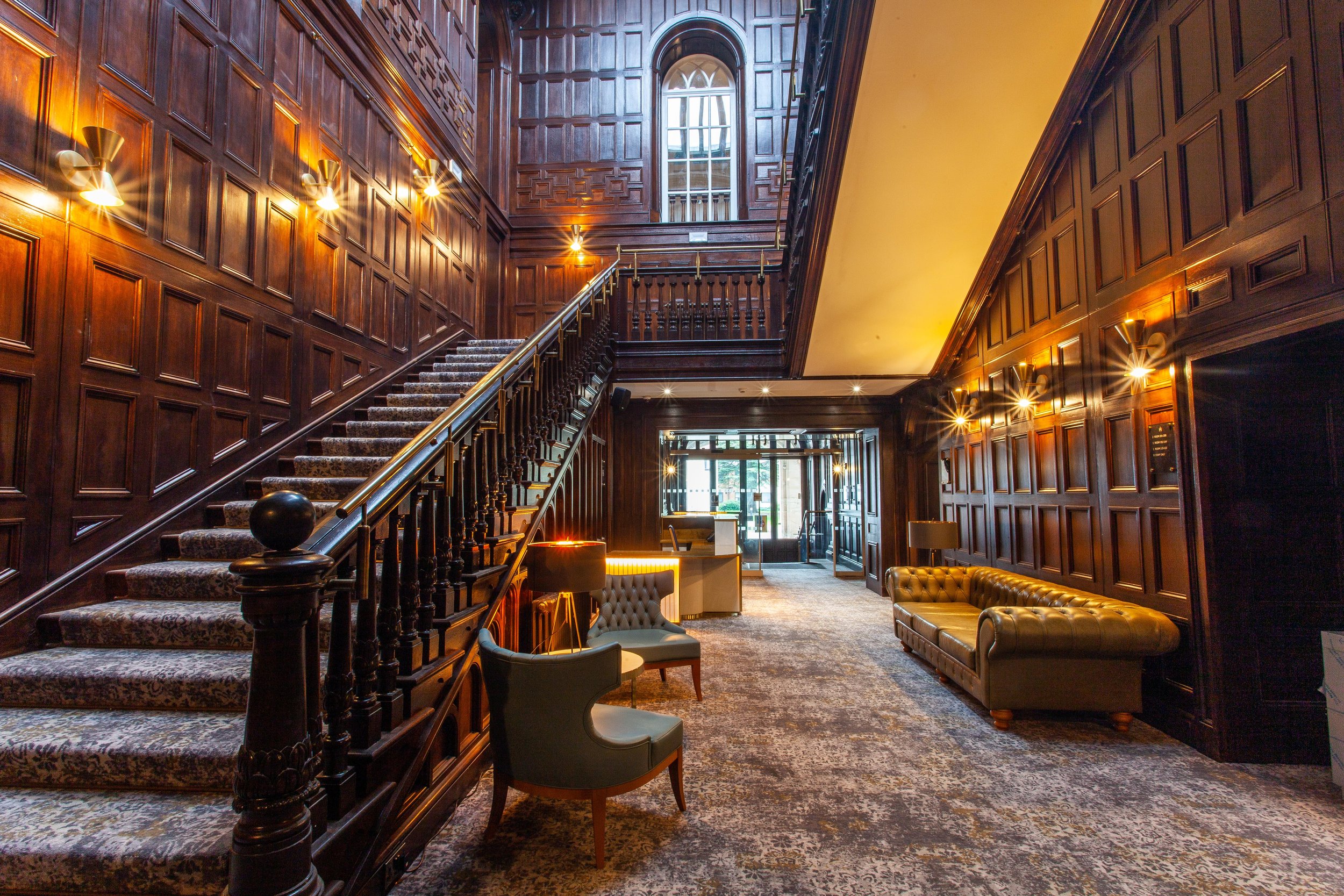 Elegant hotel lobby with wooden staircase, plush seating, and decorative paneling.