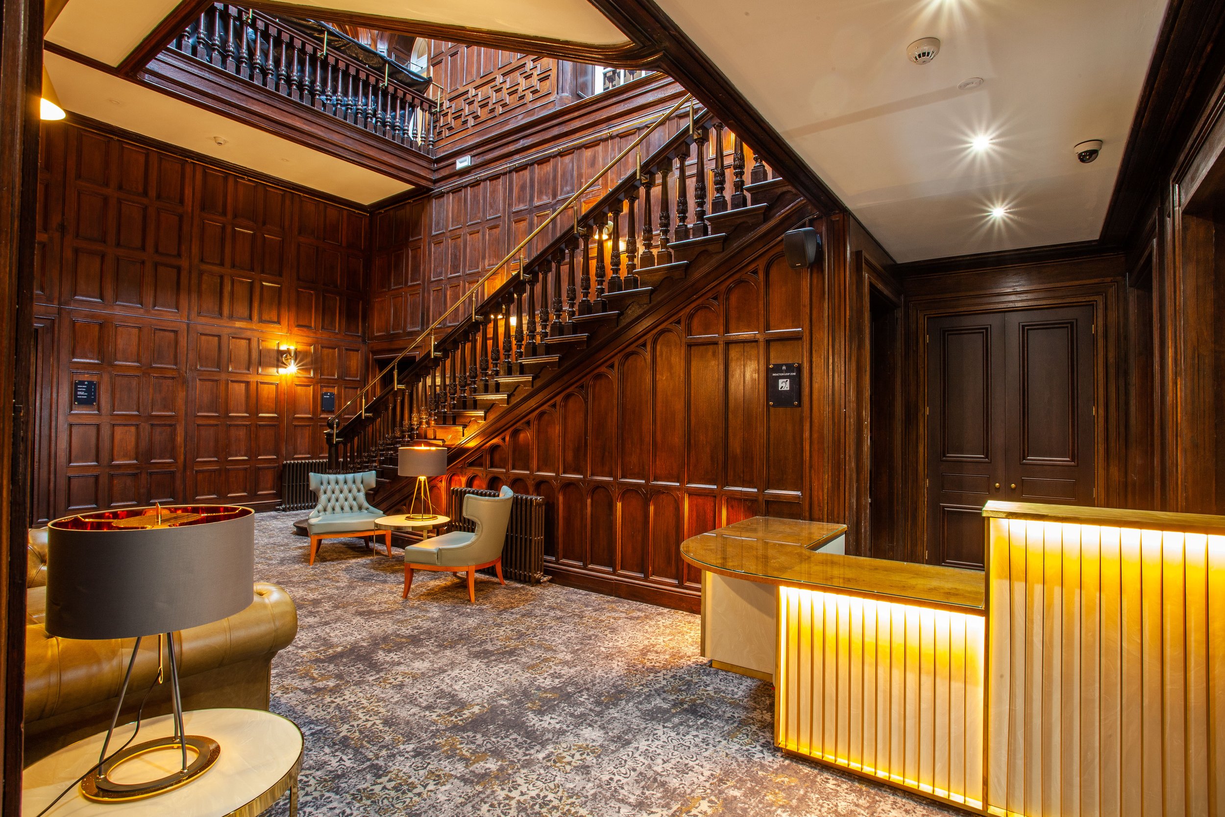 Elegant interior with wooden paneled walls, a staircase, and modern furniture including chairs and tables with lamps.