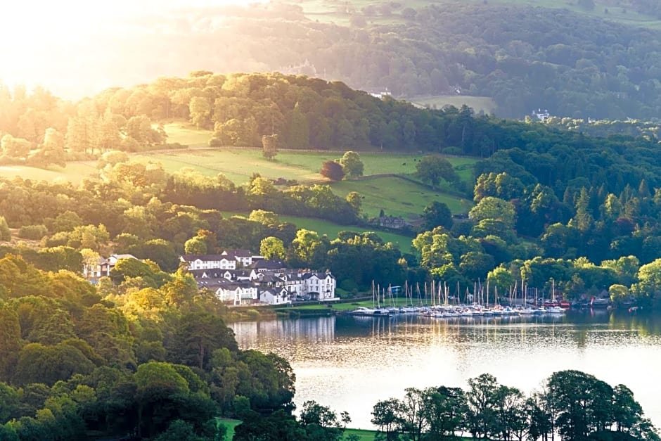 Scenic landscape with lush green hills, a cluster of white buildings, and a lake in the foreground with sailboats docked.