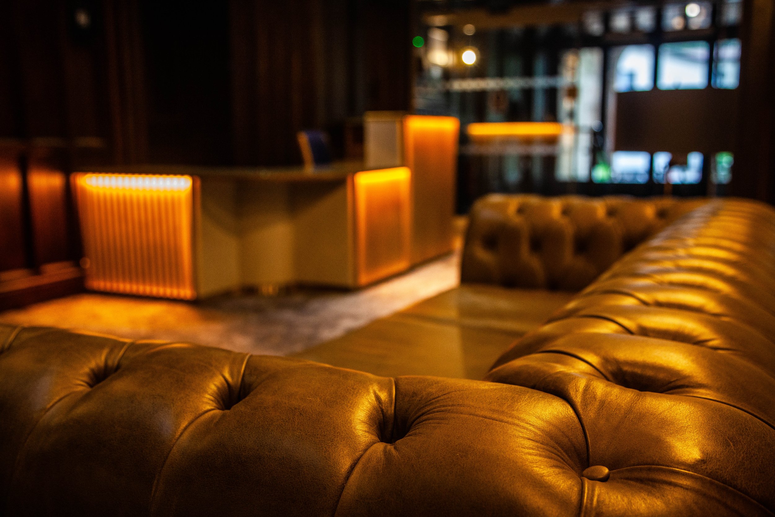 Luxurious interior with brown tufted leather sofa, warm ambient lighting, modern decor, and soft carpet.