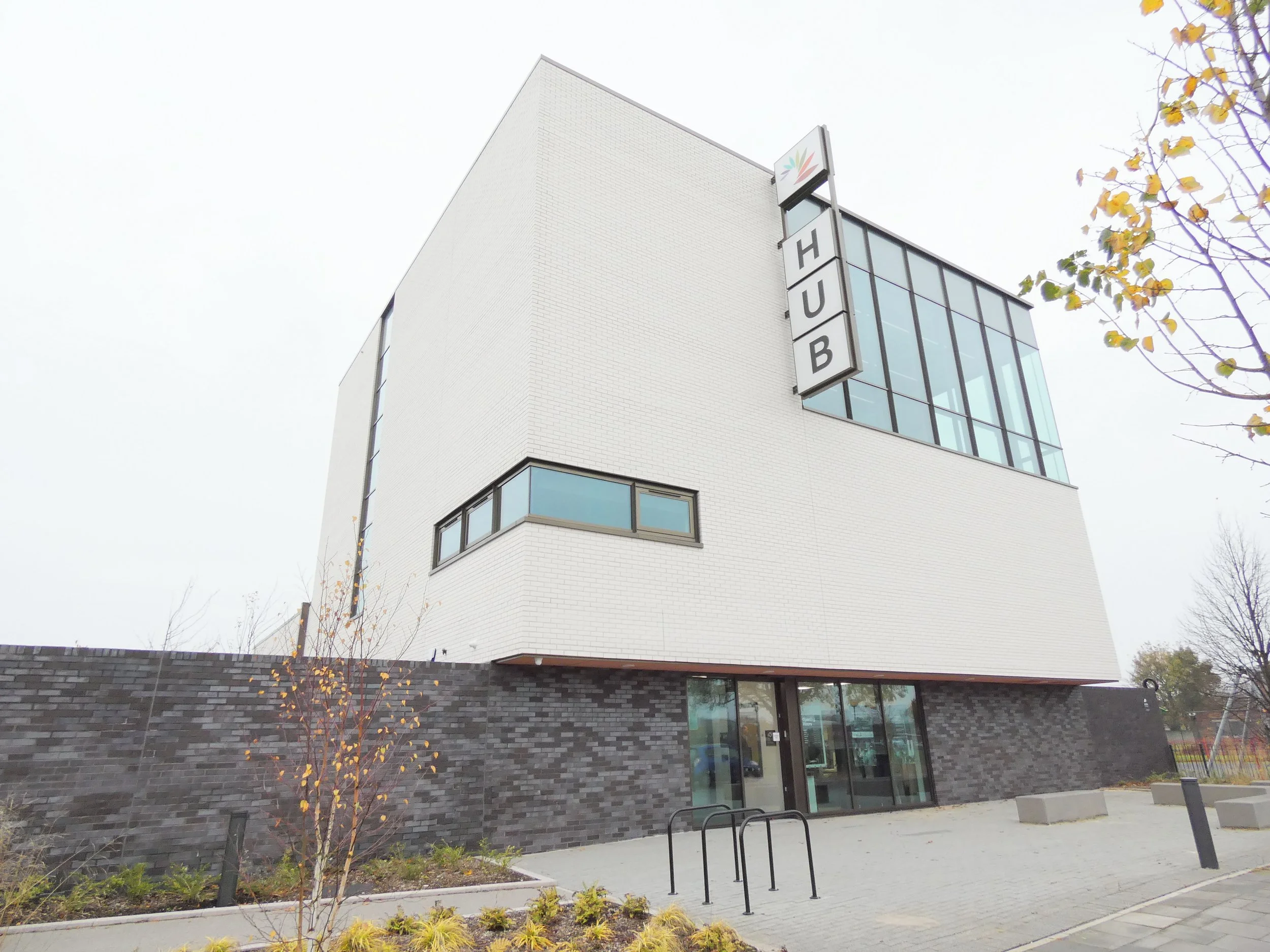 Modern building with "HUB" sign, featuring large windows and a brick facade, surrounded by trees and plants.