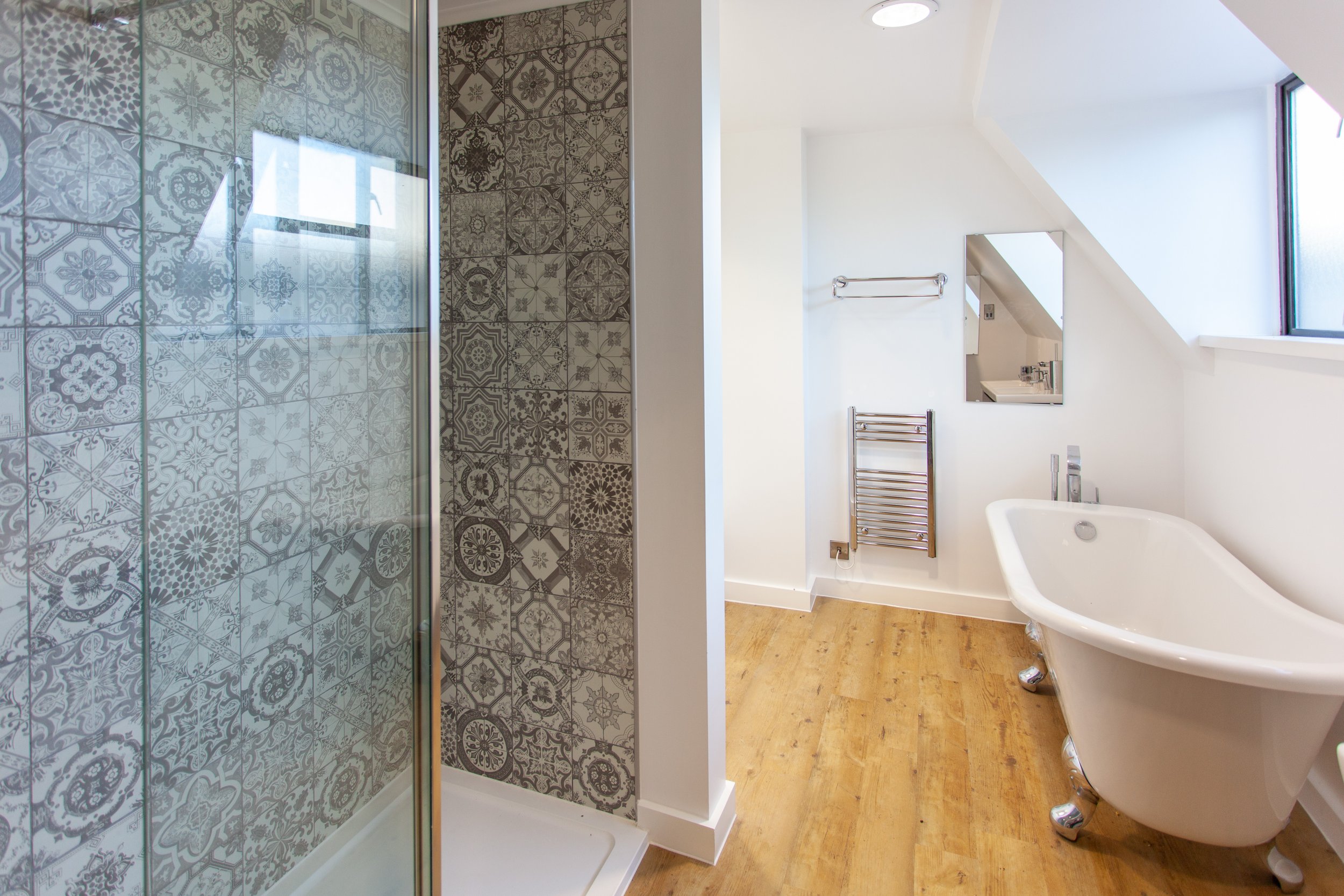 Bathroom with clawfoot bathtub and patterned tile shower, wooden flooring, towel rack, and mirror.