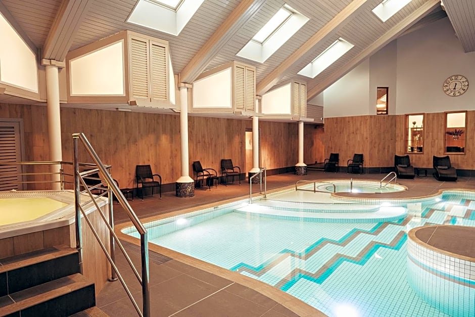 Indoor swimming pool with modern design, featuring a hot tub and lounge chairs under a high ceiling with skylights.
