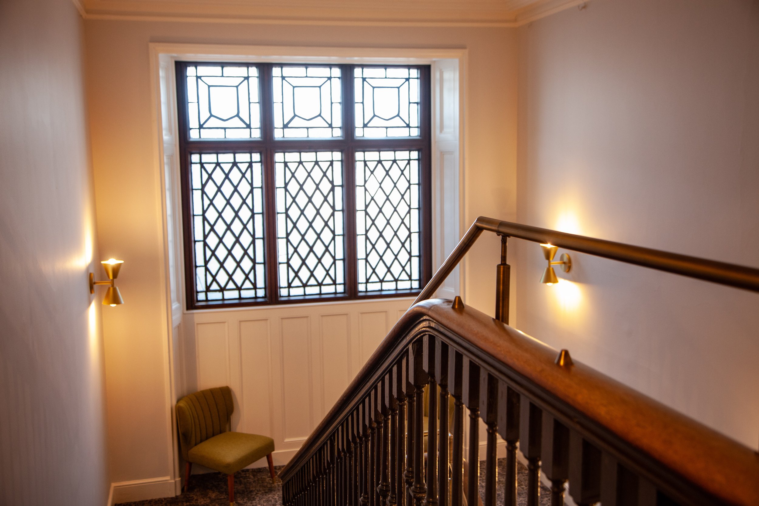 Interior staircase with wooden banister, decorative window, and green upholstered chair
