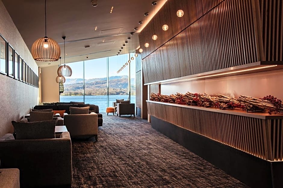 Modern lounge area with sofas, large windows with scenic view, wooden decor, and hanging lights.