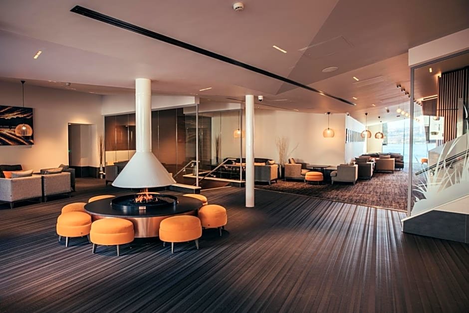 Modern lounge area with seating and central fireplace; features orange stools and contemporary decor.