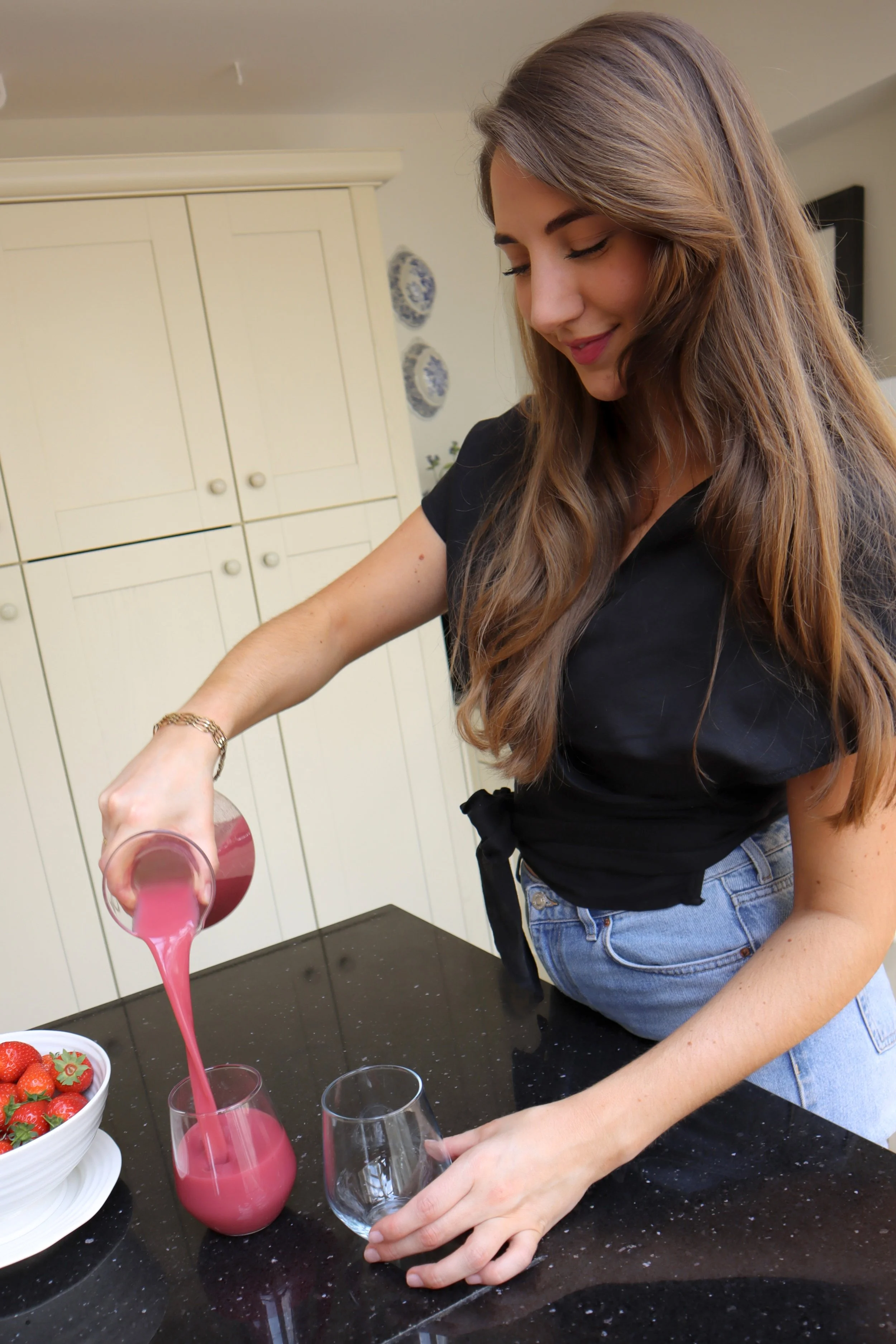 Amy Follows pouring pink smoothie into a glass in a kitchen.