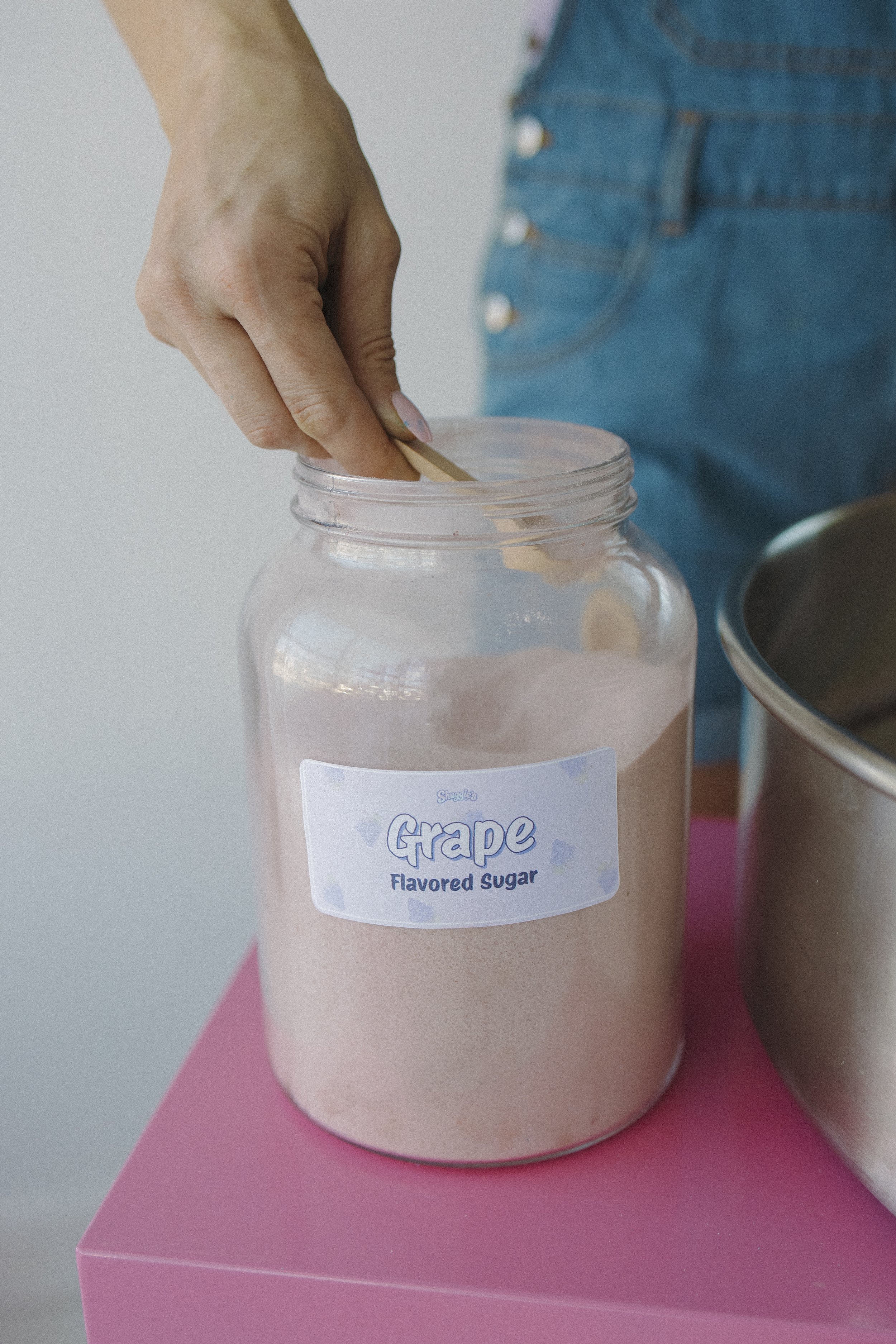 A glass jar labeled 'Grape Flavored Sugar' with pink powdered ingredient inside, placed on a pink surface.