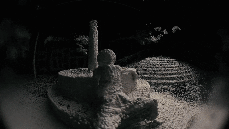 Snow-covered garden statue of a cherub sitting on a ledge during night time.