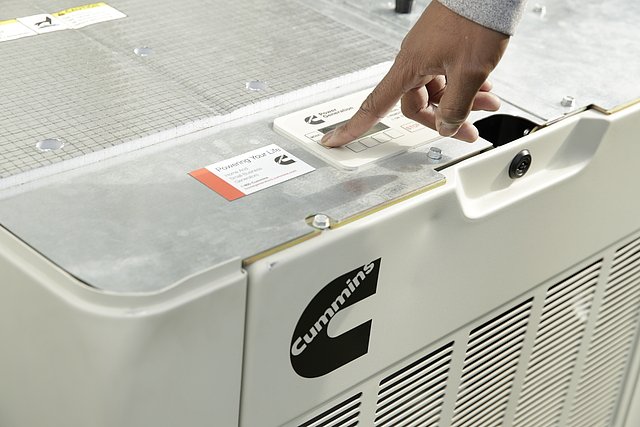 A hand pressing the power button on a Cummins generator.