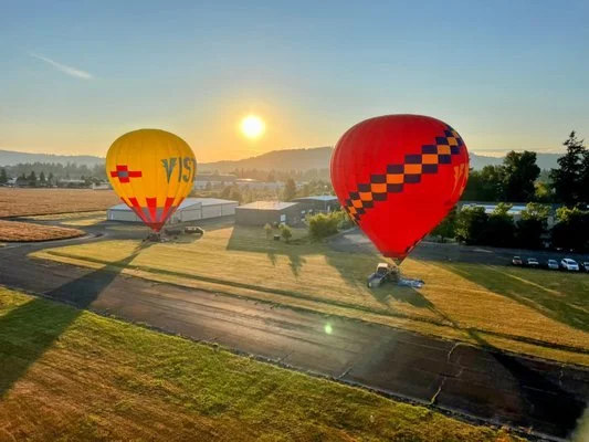 Two hot air balloons, one yellow and one red, floating over a field during sunrise.